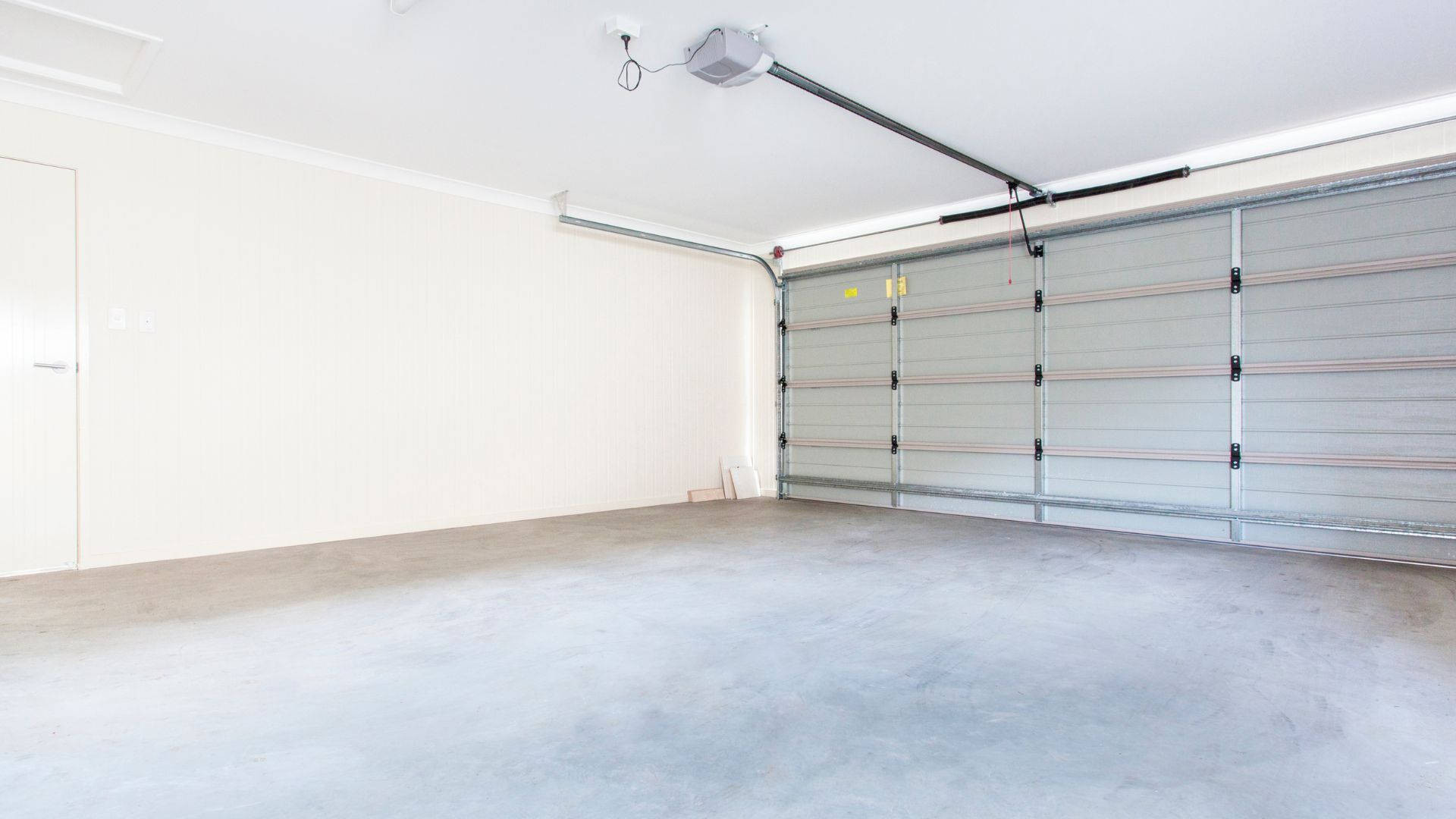 room 桌布 壁紙 — 空置清潔的車庫，混凝土地板，關閉的分段門，上方有明亮的燈光。