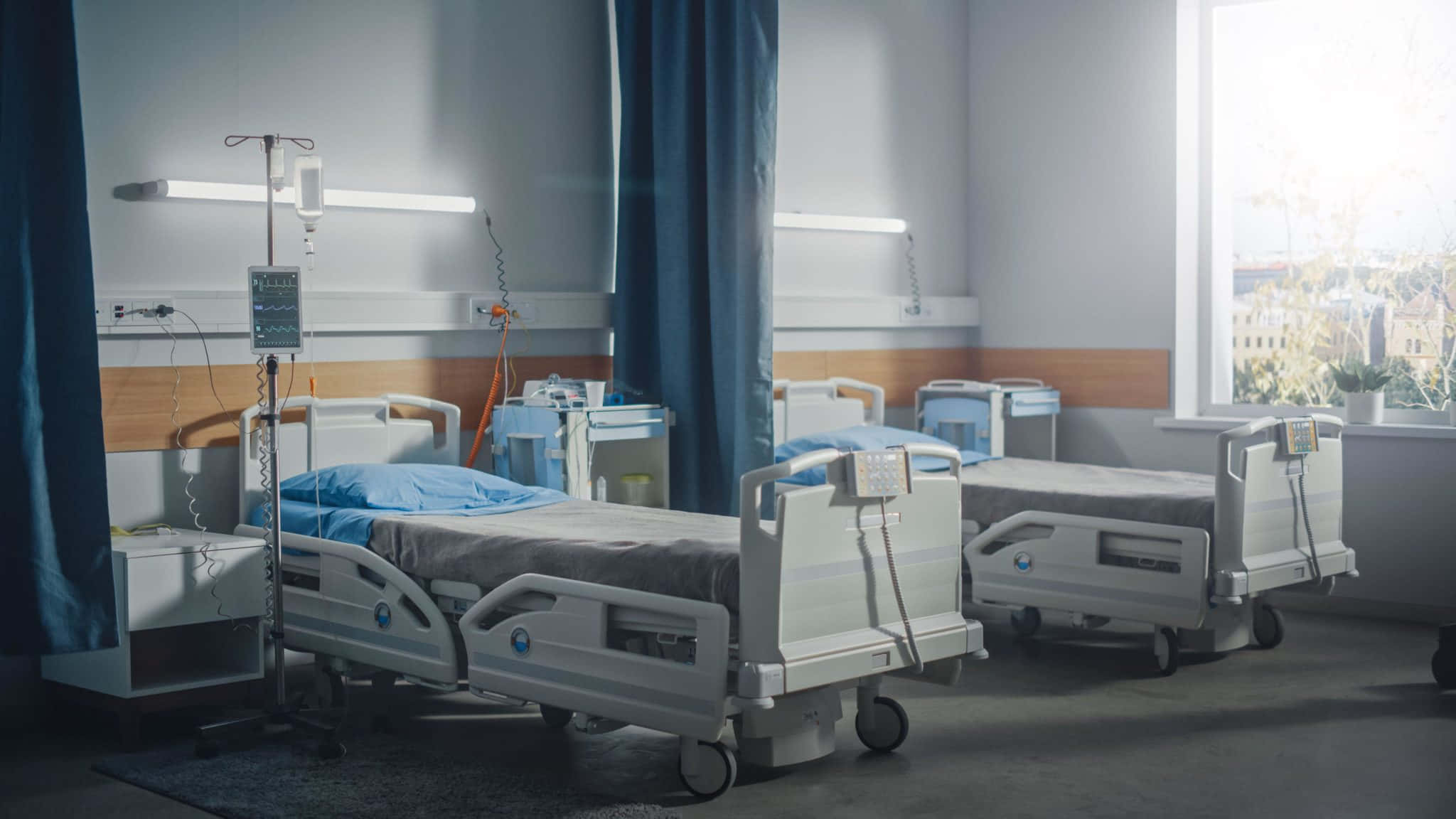 Hospital 桌布 壁紙 — 空置的醫院病房，內有醫療床和設備，窗戶透入柔和自然光。