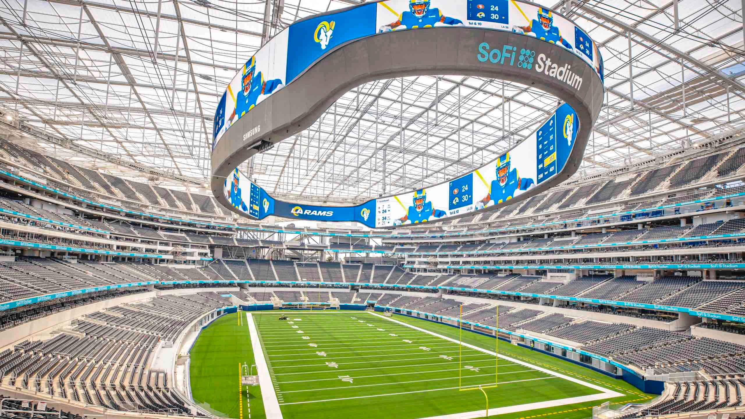 Sofi Stadium 桌布 壁紙 — 空蕩蕩的SoFi體育場的鳥瞰圖，展示了其巨大的弧形視頻板和玻璃屋頂下充滿活力的綠色足球場。