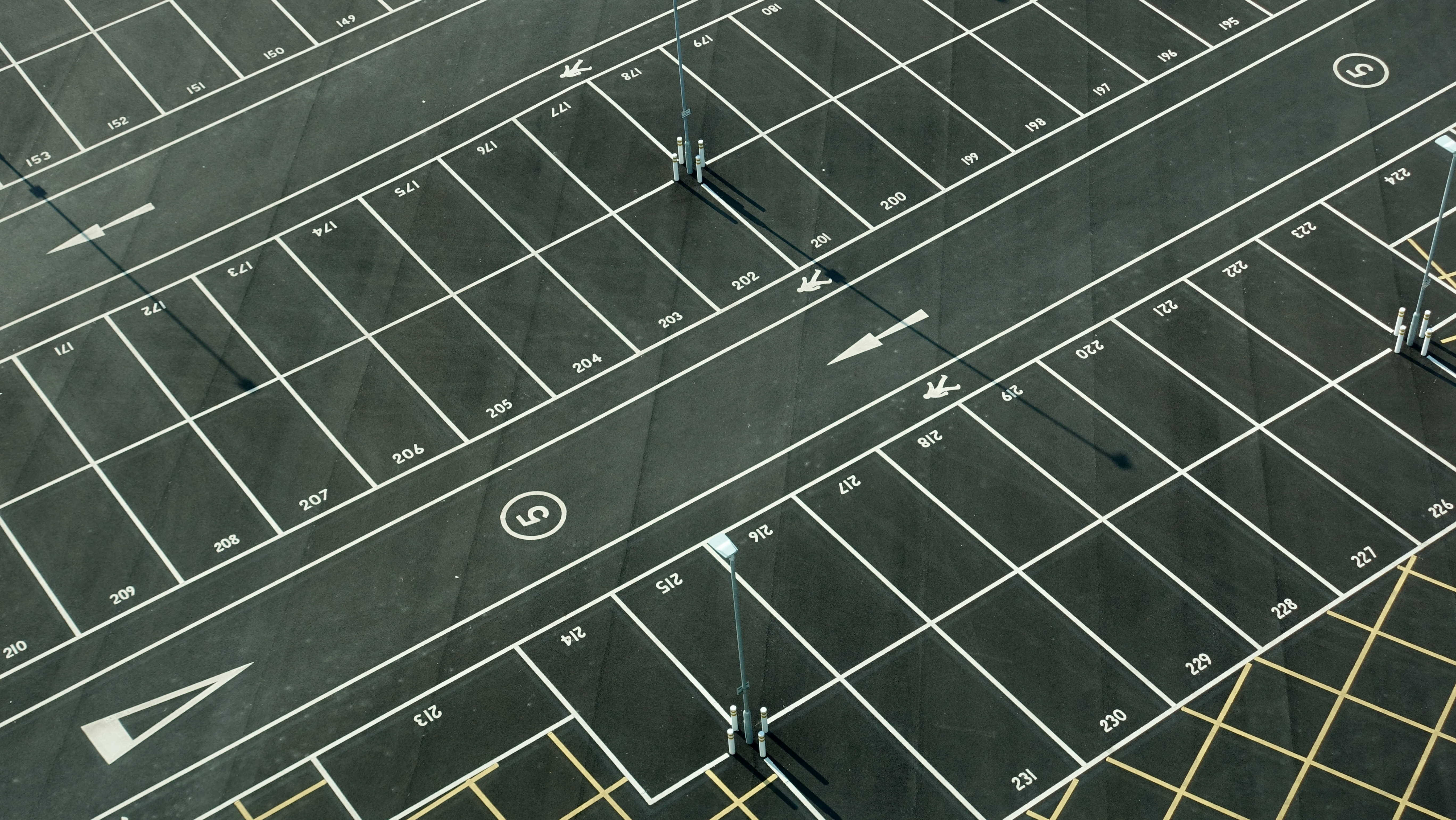 Road 桌布 壁紙 — 空蕩蕩的瀝青停車場鳥瞰圖，帶有白色編號線和方向箭頭，在明亮的日光下。