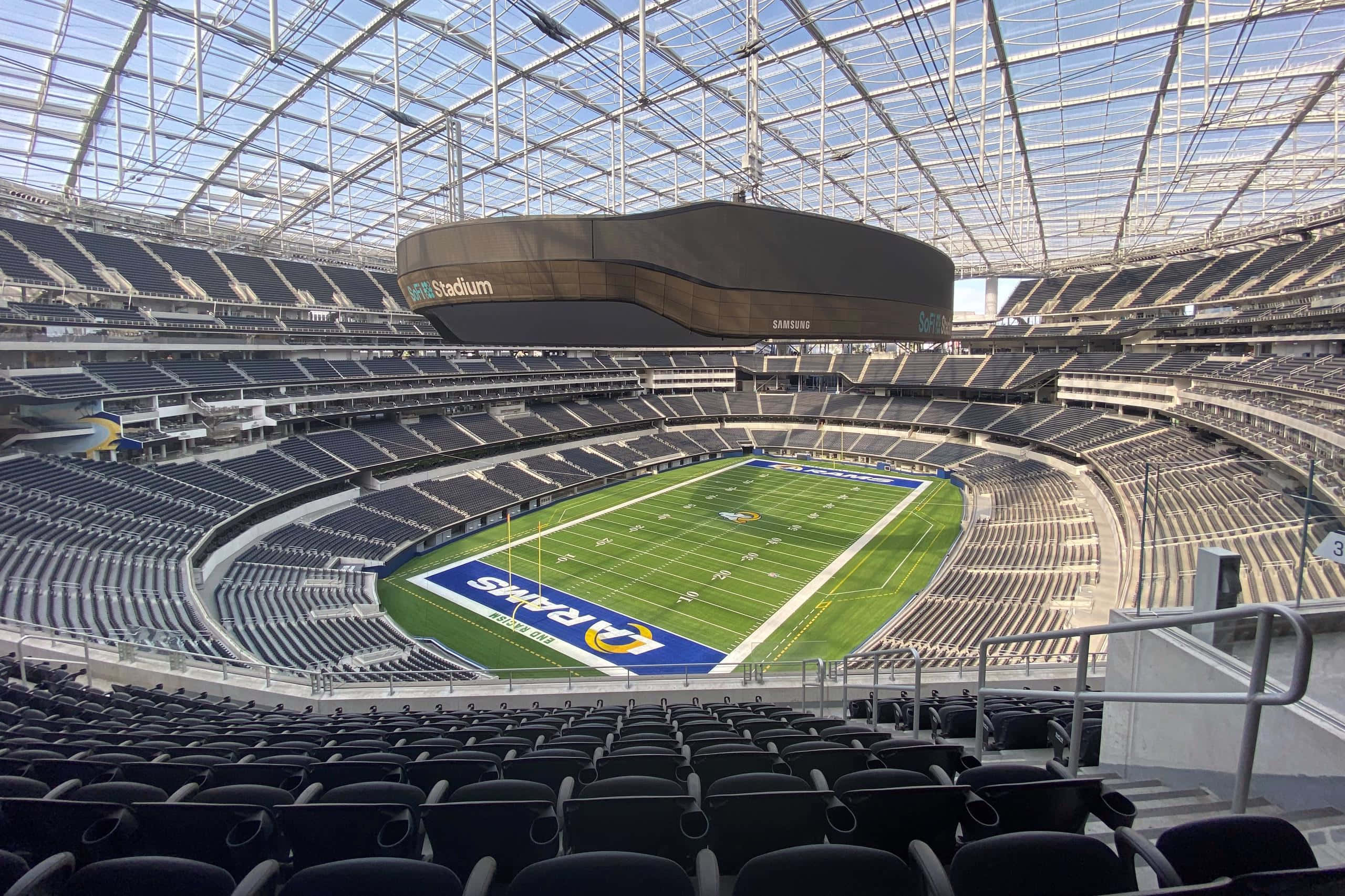 Sofi Stadium 桌布 壁紙 — 空蕩蕩的現代足球場鳥瞰圖，綠色球場和黑色座椅在玻璃屋頂下。