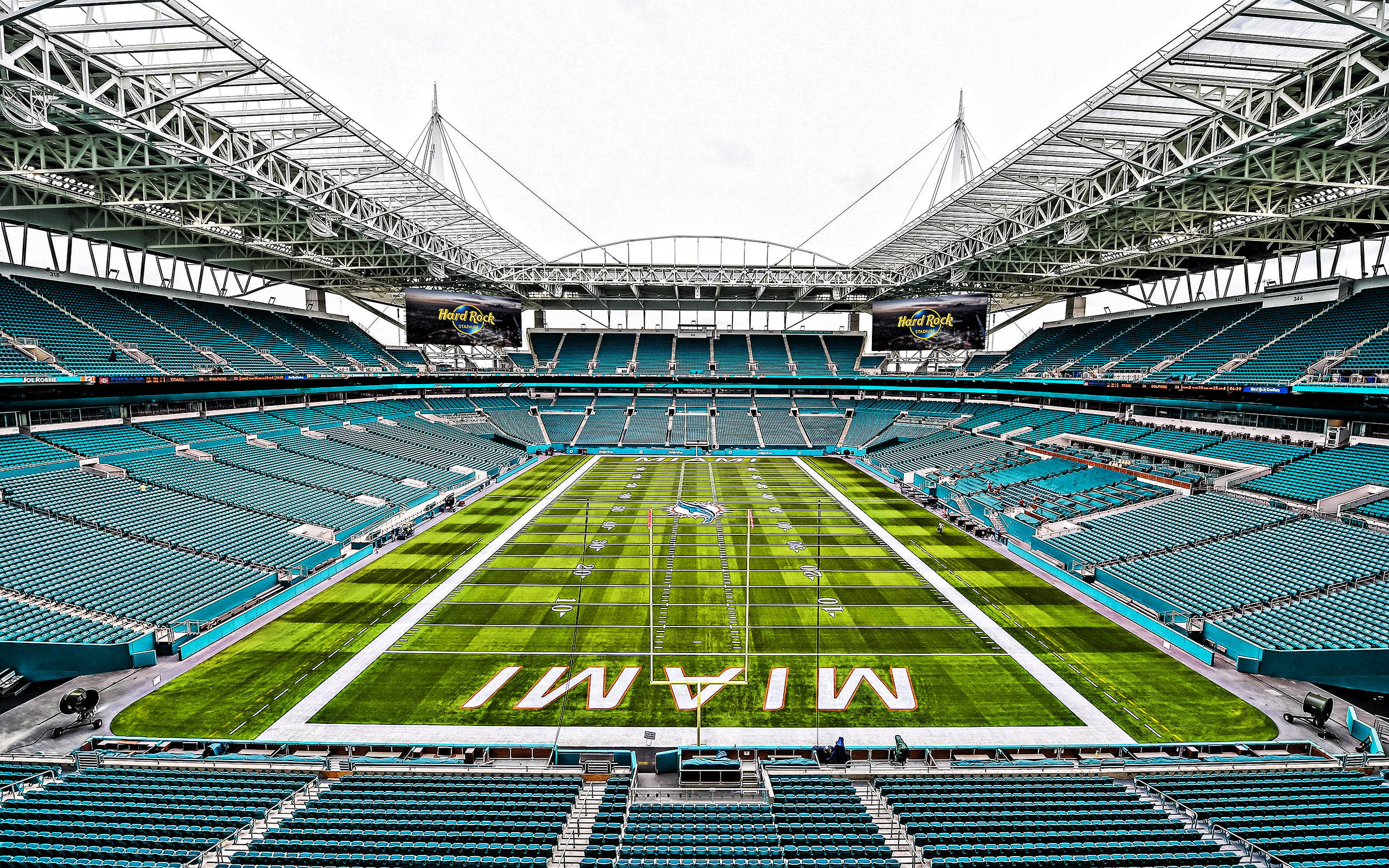 Stadium 桌布 壁紙 — 空蕩蕩的邁阿密足球場的鳥瞰圖，擁有鮮綠色的草坪和藍綠色座椅，天空多雲。