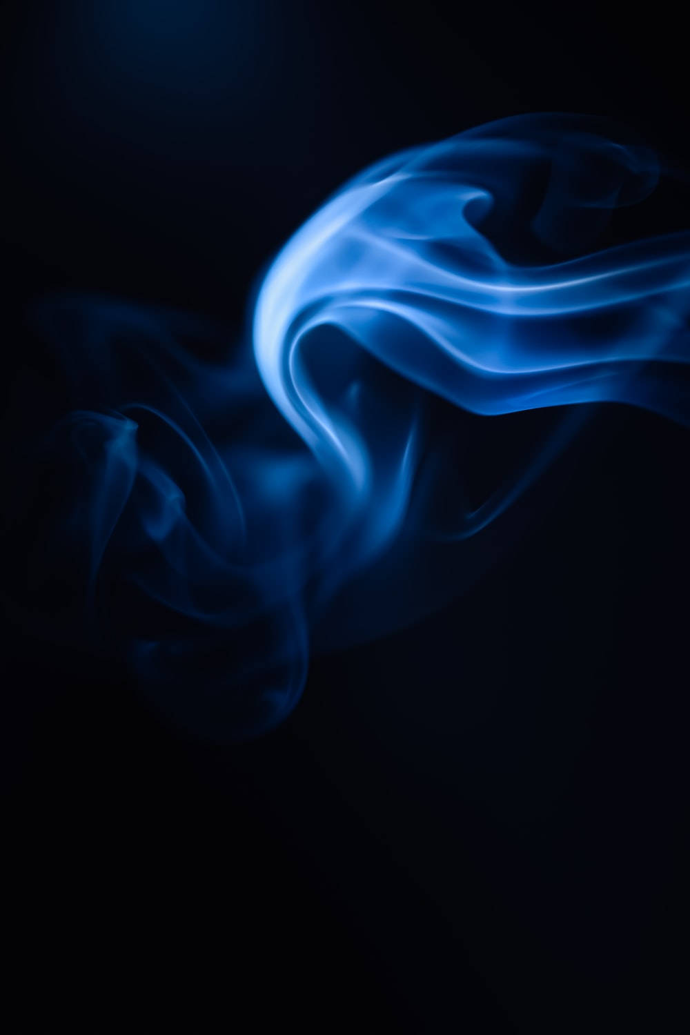 藍色 桌布 壁紙 — 空靈的藍色煙霧在深黑色背景上優雅地盤旋，形成迷人的抽象形態。