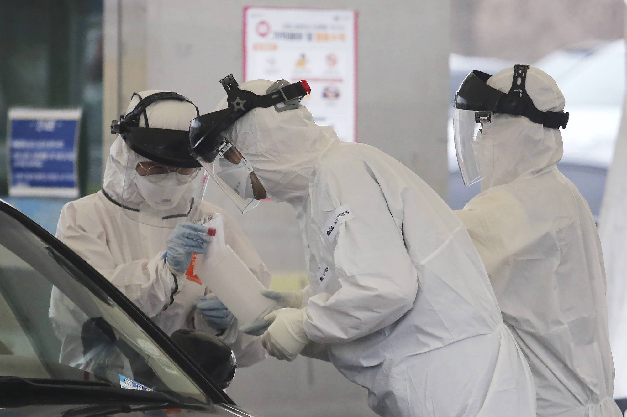 Coronavirus 桌布 壁紙 — 穿著全套白色防護衣和面罩的醫護人員在免下車檢測站從車窗收集樣本。