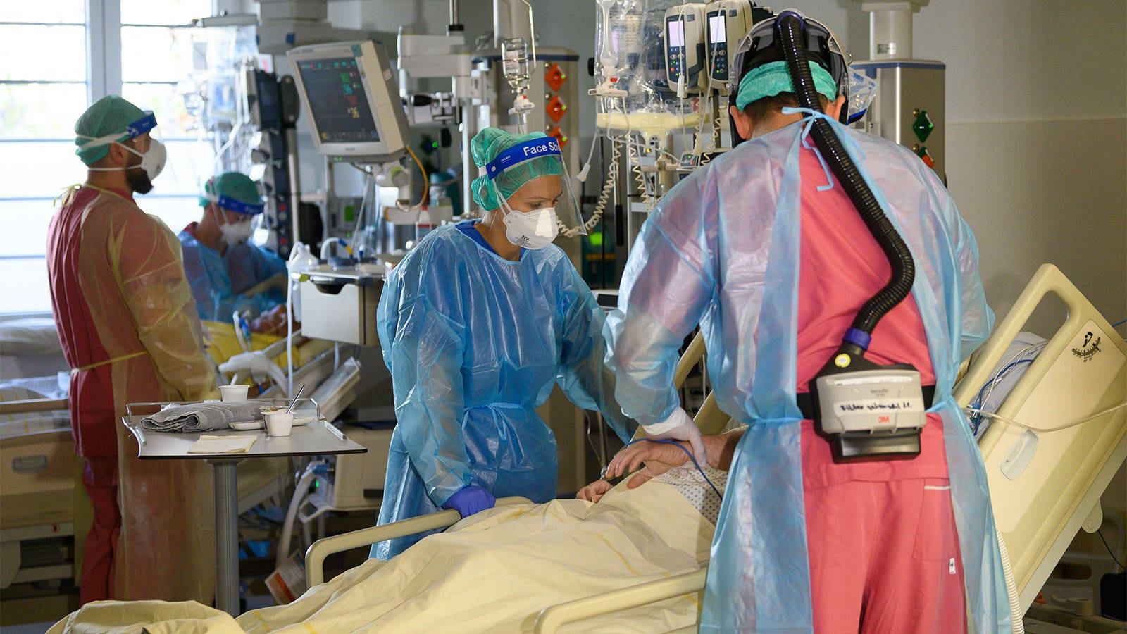 Surgeon 桌布 壁紙 — 穿著全套防護裝備的醫護人員在繁忙的醫院加護病房照顧病人，病房內佈滿監測儀器和設備。