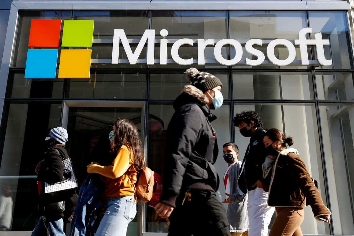 在陽光明媚的日子裡，戴著口罩的行人走過微軟辦公大樓。 — Microsoft 壁紙