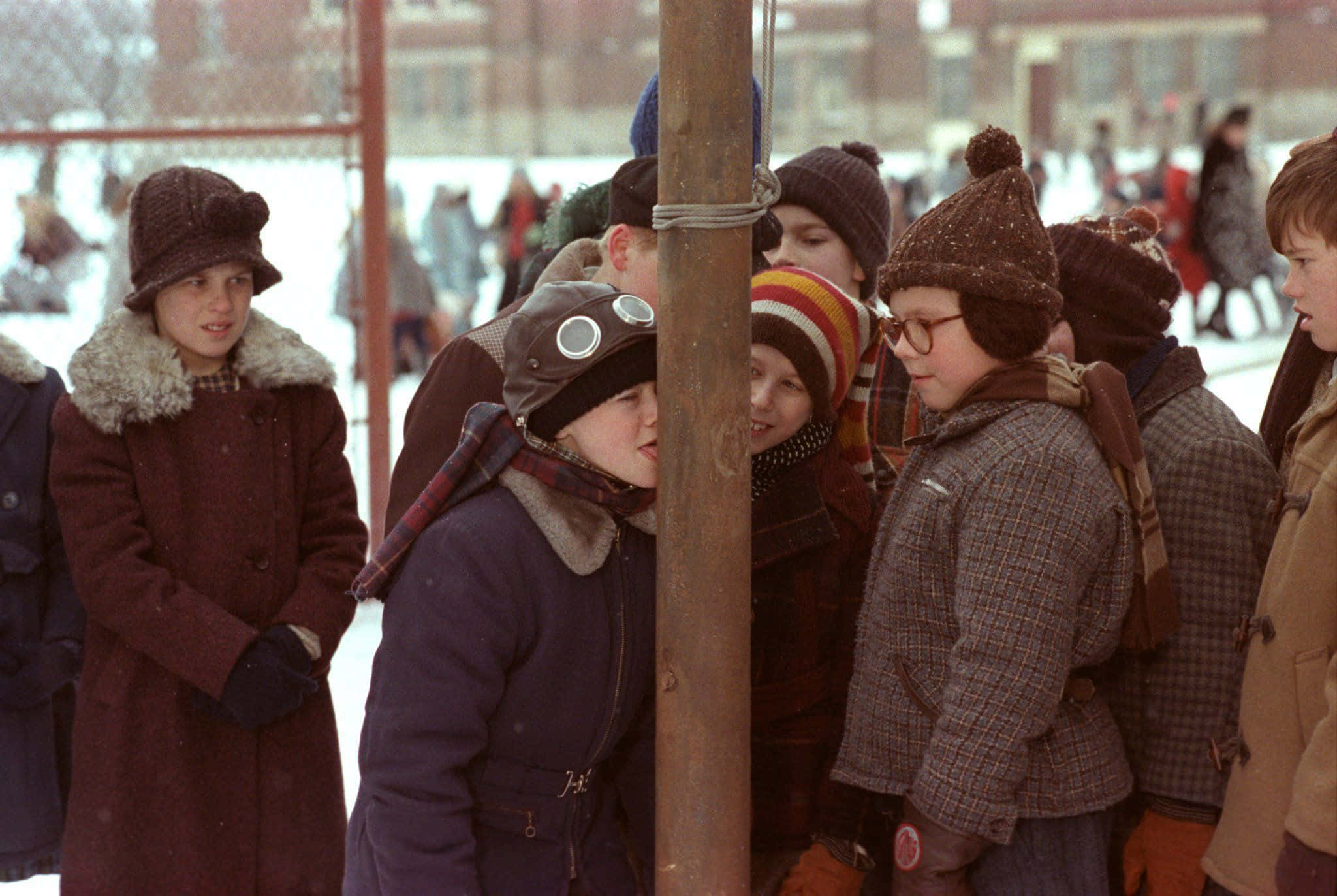 a christmas story 桌布 壁紙 — 穿著冬季外套和帽子的孩子們聚集在雪地戶外場景中的一根木柱周圍。