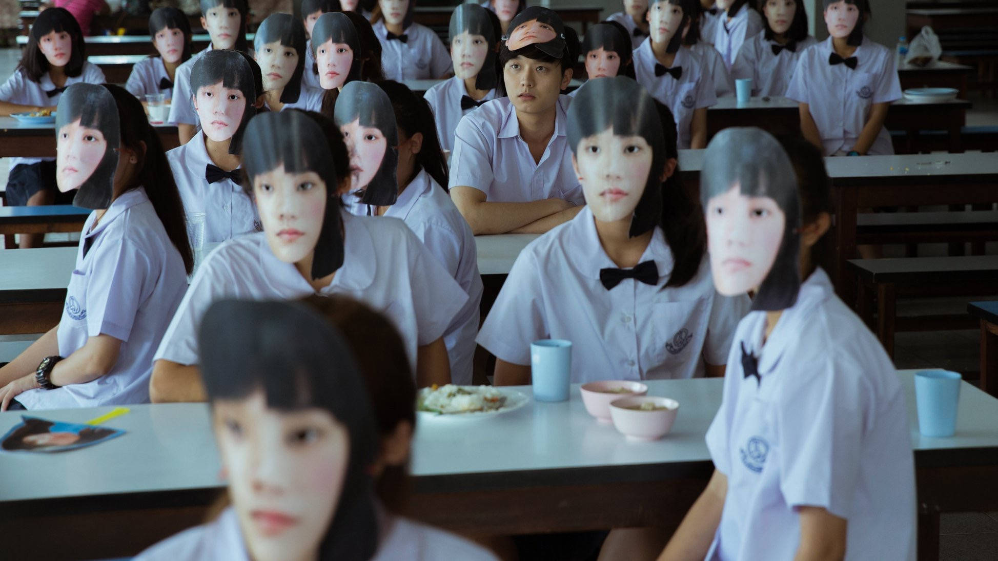 高清 桌布 壁紙 — 穿著制服的學生坐在教室裡，令人不安地戴著一模一樣的面罩，遮蓋了他們的表情。