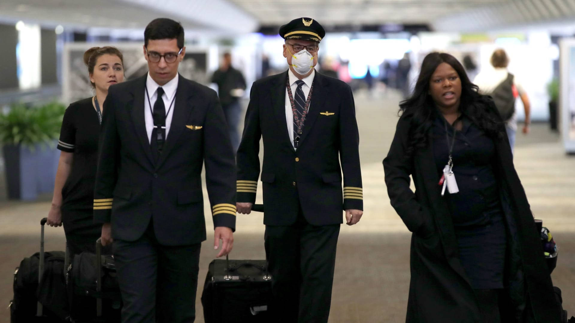 Airport 桌布 壁紙 — 穿著制服的機組人員拖著滾輪行李箱走過光線明亮的機場航廈。