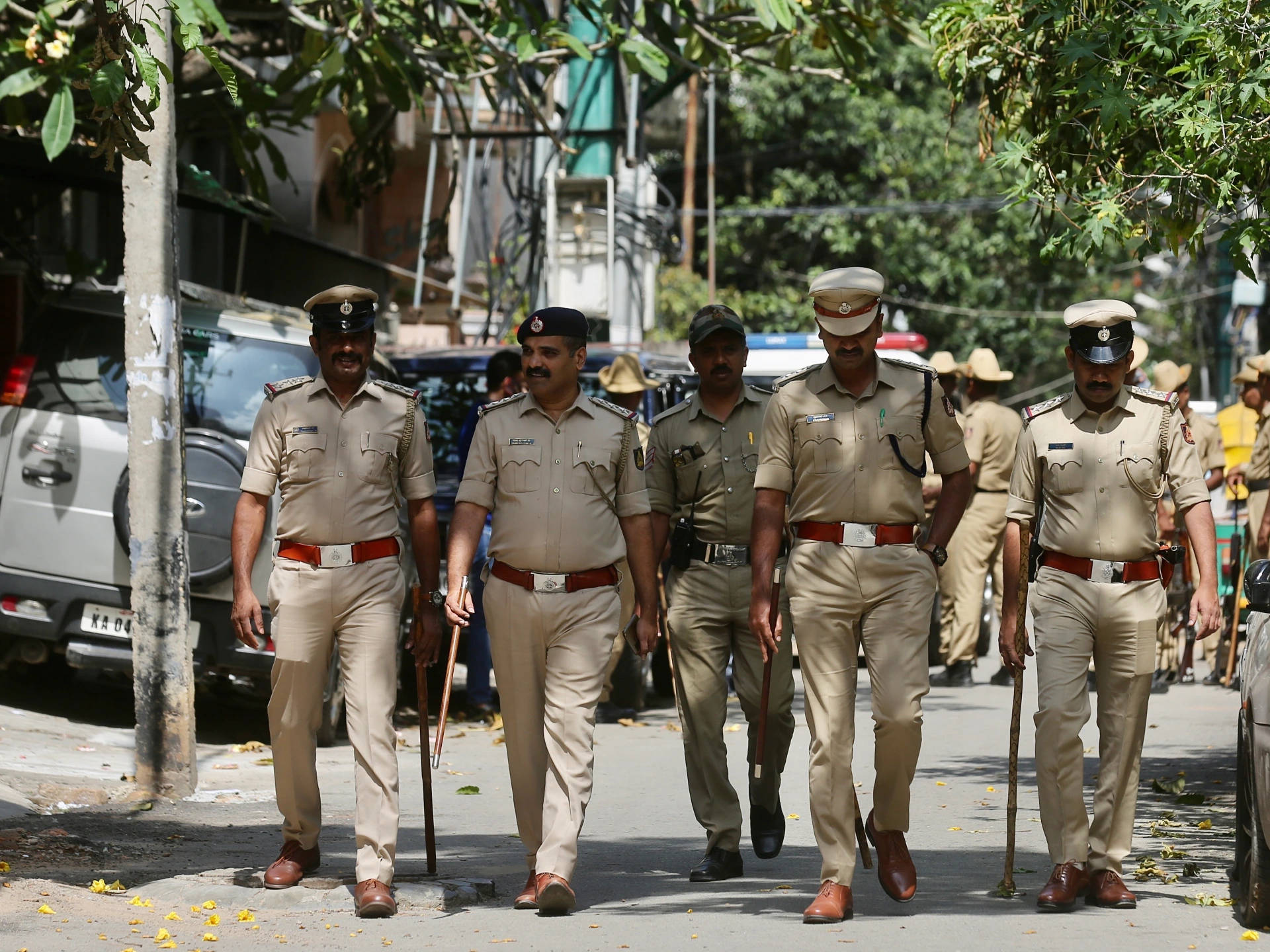 Indian 桌布 壁紙 — 穿著卡其色制服的警察在明亮的日光下自信地走在綠樹成蔭的城市街道上。