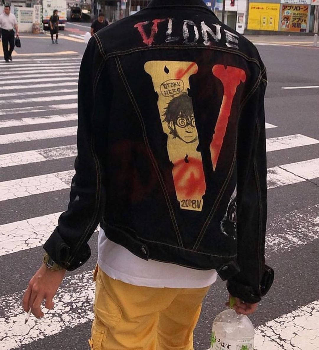 Vlone 桌布 壁紙 — 穿著印有大型動漫圖案黑色牛仔外套的人，從背面看正在穿過城市行人穿越道。