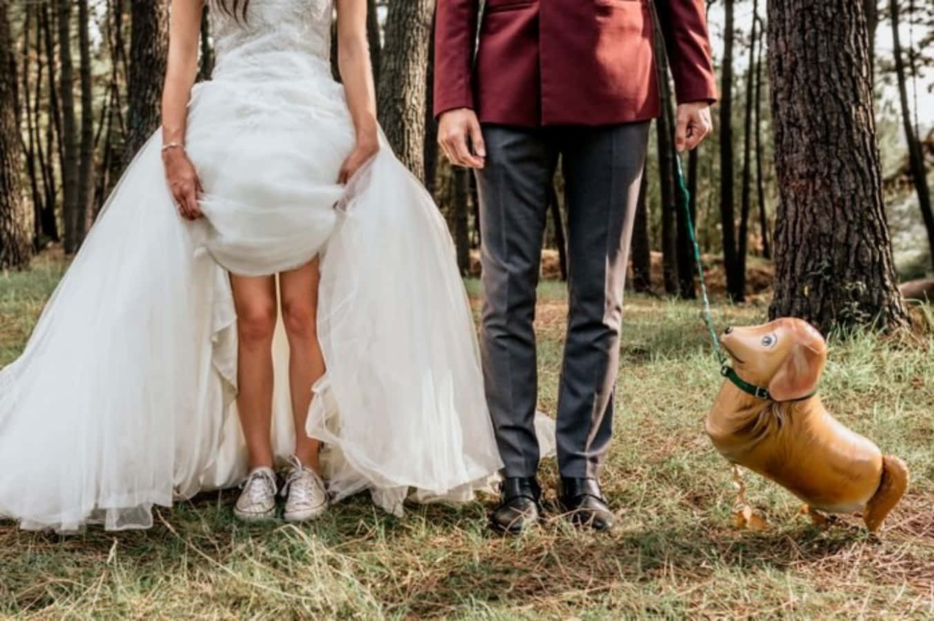 Funny Wedding 桌布 壁紙 — 穿著婚紗禮服的新娘和新郎站在森林中，用皮帶牽著一個臘腸狗氣球。