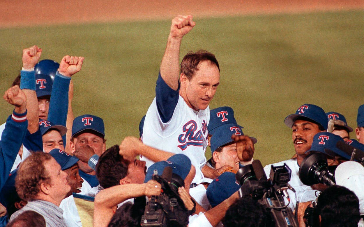 Nolan Ryan 桌布 壁紙 — 穿著德州遊騎兵隊球衣的棒球教練和球員在佈滿攝影機的場地上高舉拳頭慶祝勝利。