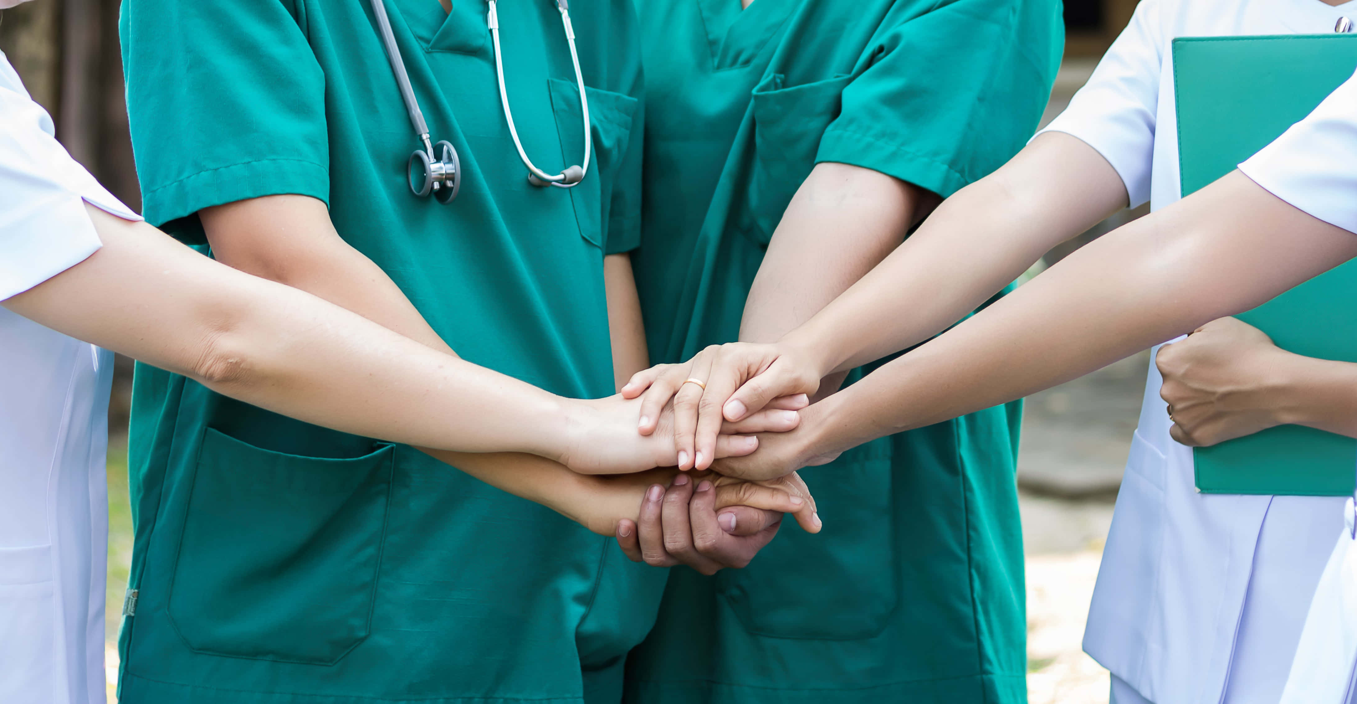 Nursing 桌布 壁紙 — 穿著手術衣的醫療專業人員將手圍成一個圓圈，象徵團隊合作與關懷。