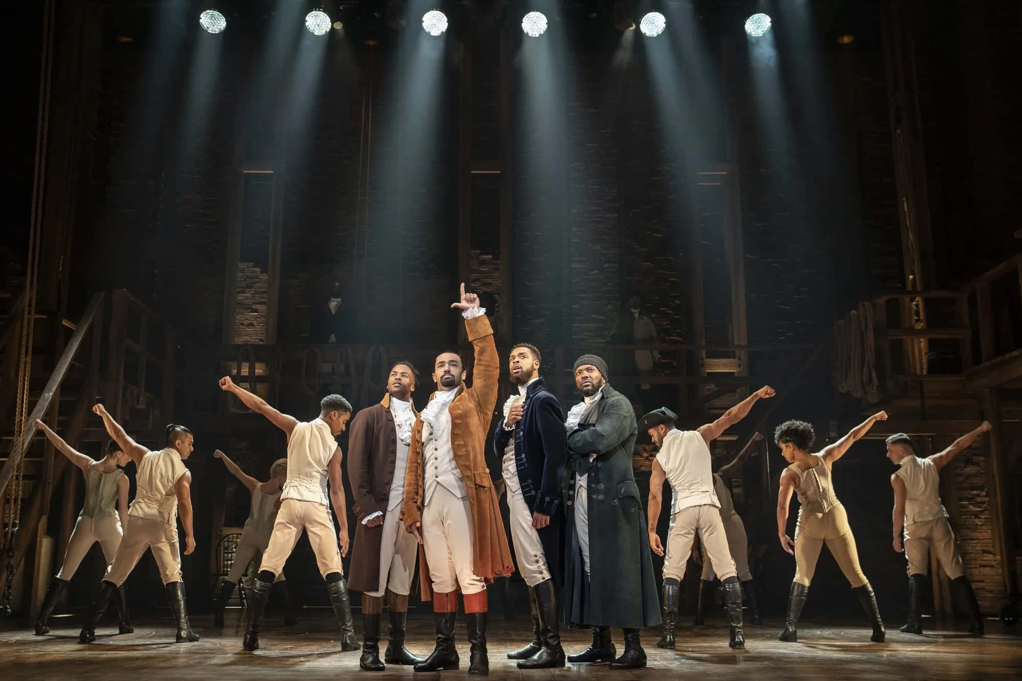 Hamilton 桌布 壁紙 — 穿著殖民時期服裝的劇院表演者在質樸的舞台上，在戲劇性的聚光燈下擺出動態姿勢。