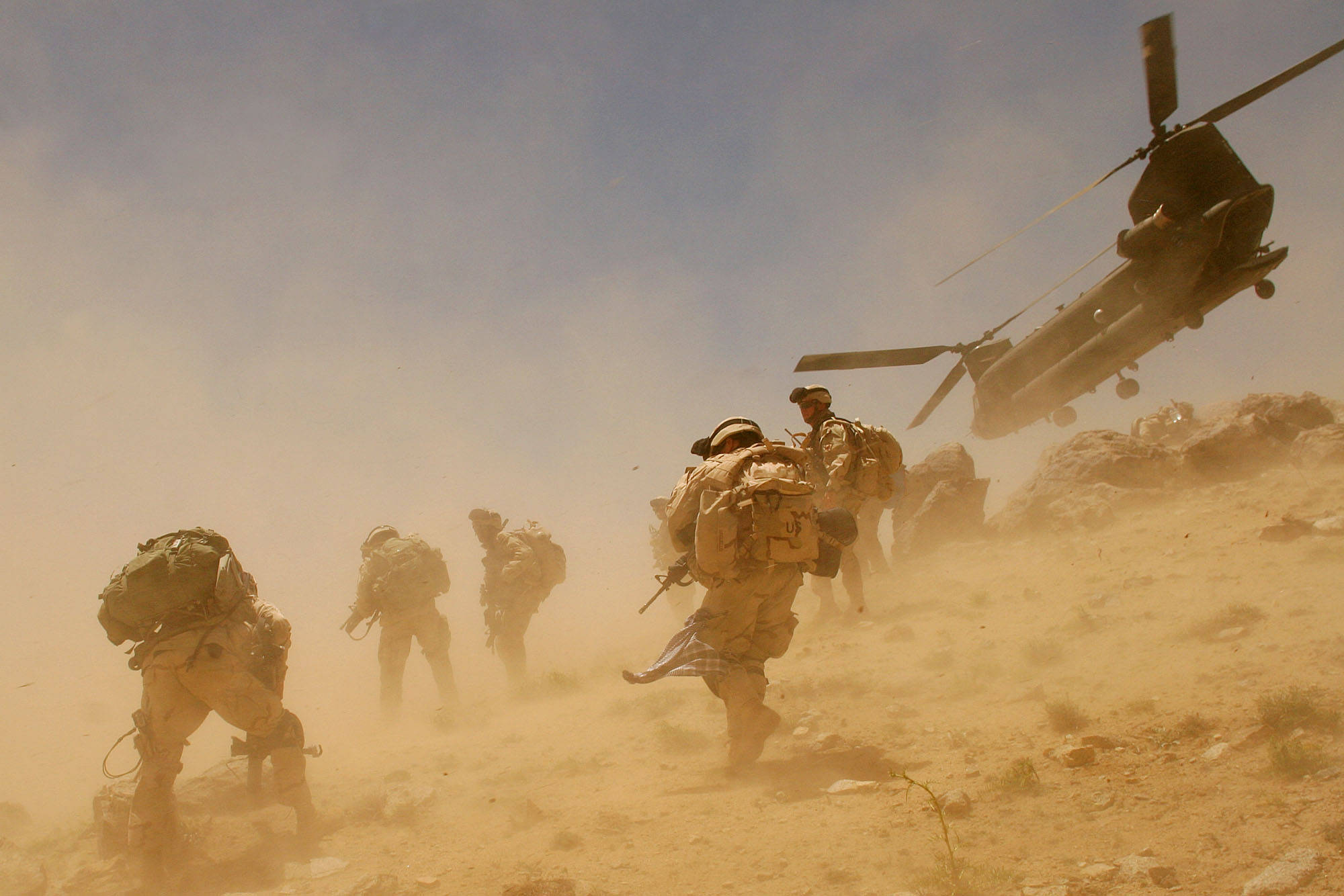 Afghanistan 桌布 壁紙 — 穿著沙漠裝備的士兵在旋轉的沙塵中衝上山坡，一架軍用直升機在頭頂盤旋。