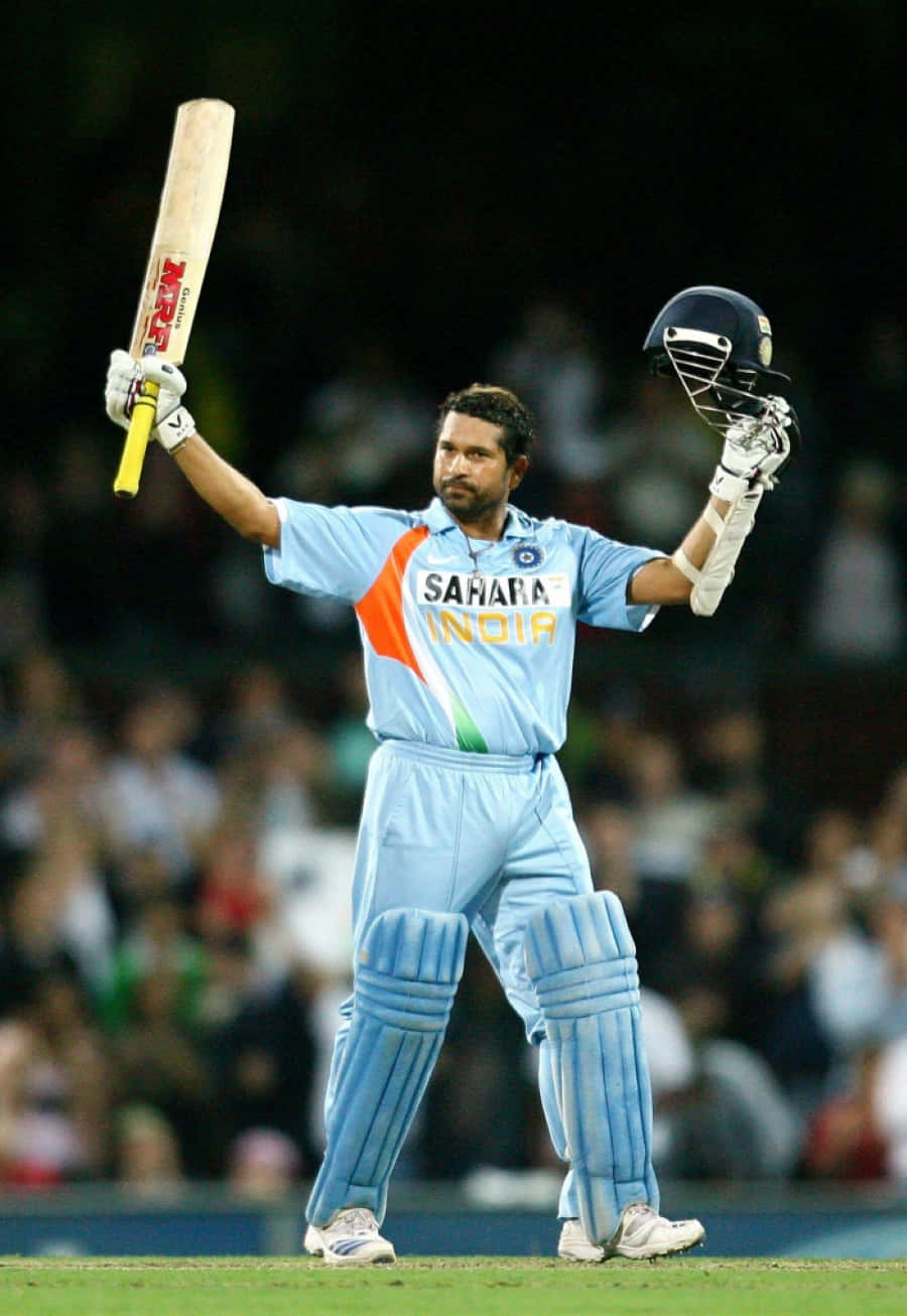 Sachin Tendulkar 桌布 壁紙 — 穿著淺藍色印度隊服的板球手在球場燈光下高舉球棒和頭盔，擺出勝利姿勢。