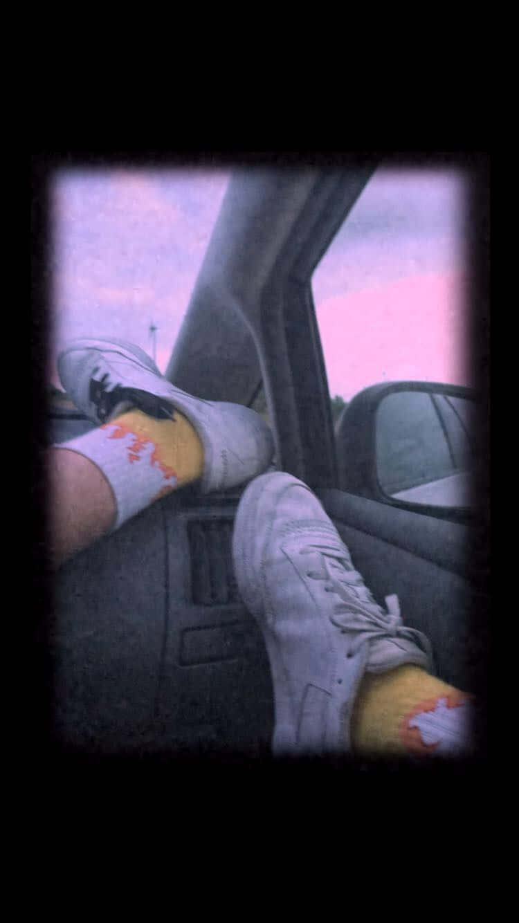 Skater Girl Aesthetic 桌布 壁紙 — 穿著白色運動鞋和圖案襪子的雙腳擱在汽車儀表板上，背景是粉紅色的暮色天空。