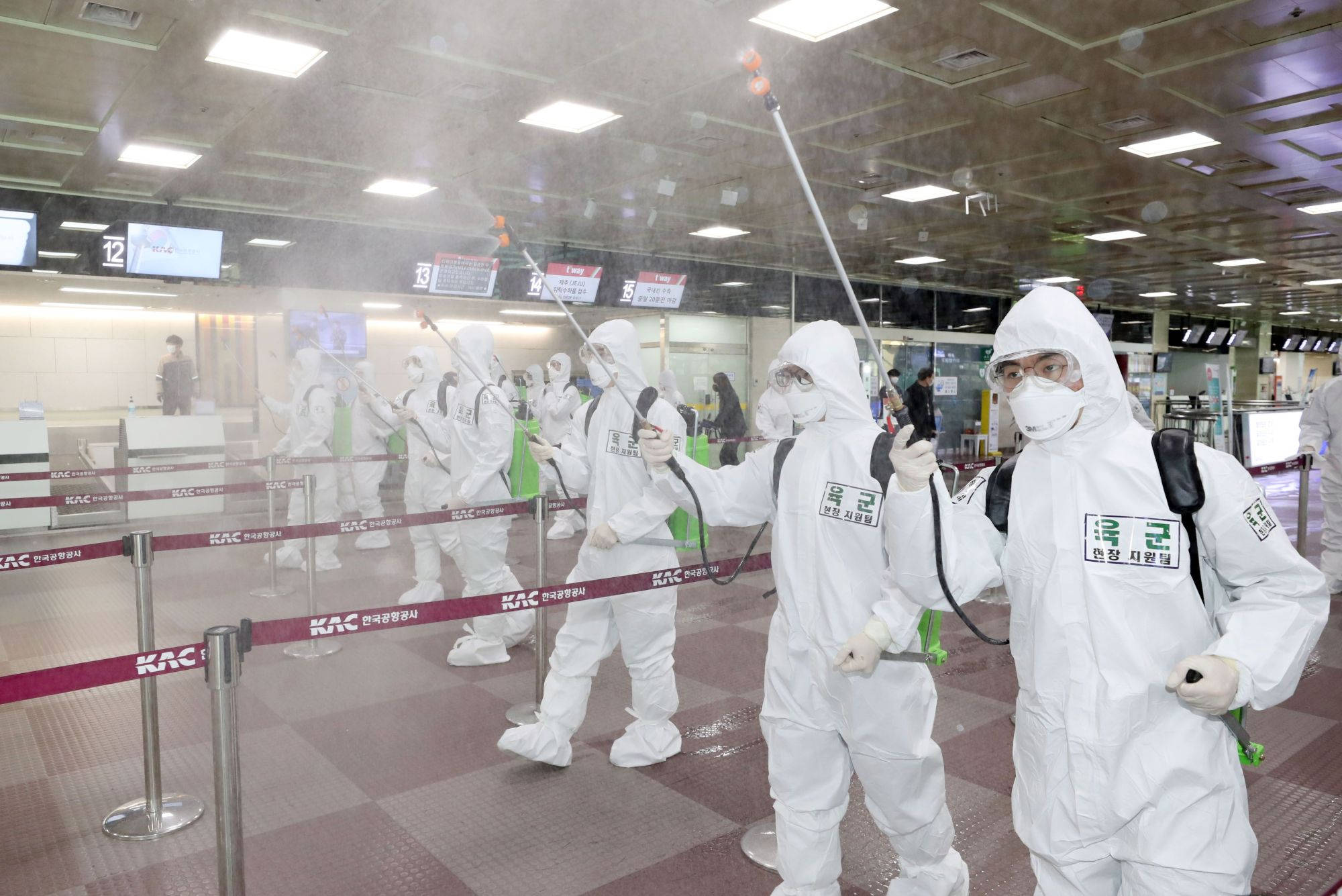 Coronavirus 桌布 壁紙 — 穿著白色防護衣的工作人員在繁忙的機場航站樓噴灑消毒劑，霧氣在空中飄浮。