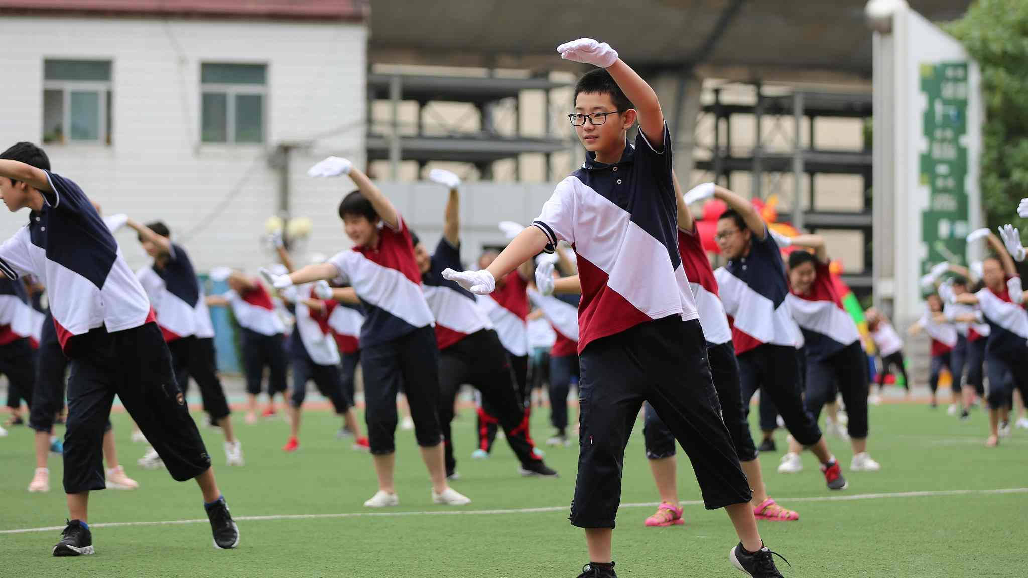 martial arts 桌布 壁紙 — 穿著相配校服的學生在日光下的綠色運動場上表演同步舞蹈動作。