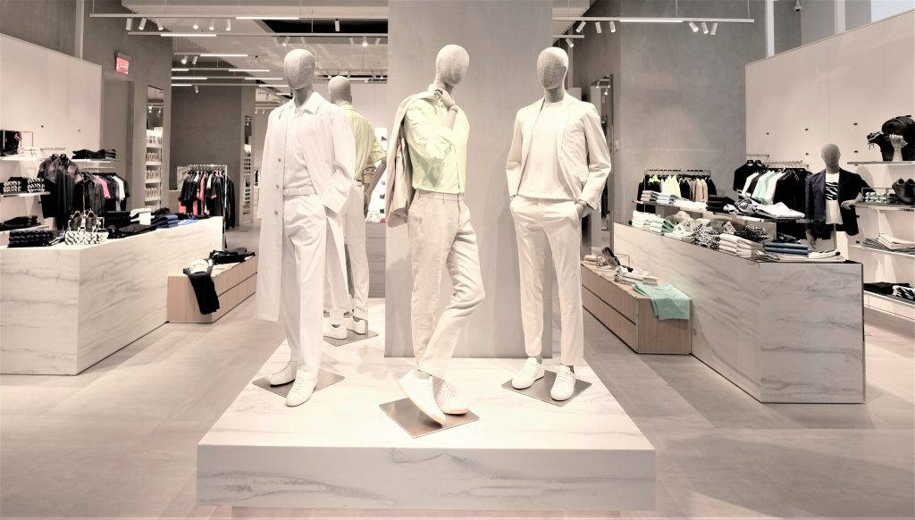 Clothes 桌布 壁紙 — 穿著簡約白色服裝的人體模型站在大理石平台上，位於線條簡潔、燈光柔和的時尚現代服裝店內。