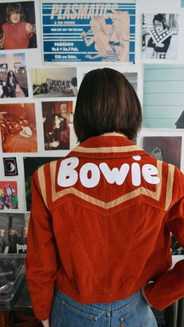 70年代動圖 桌布 壁紙 — 穿著紅色Bowie外套的人背對鏡頭，面向掛滿復古音樂海報的牆壁。