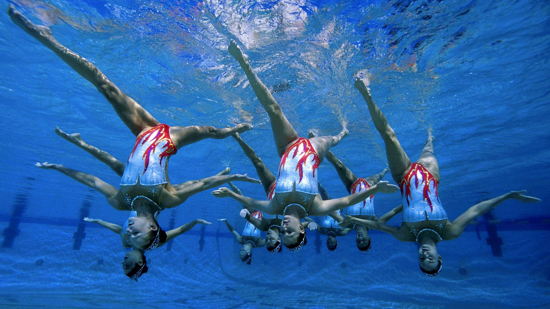 Swimming 桌布 壁紙 — 穿著紅色和白色服裝的韻律泳選手在清澈的藍色泳池中優雅地擺出水中姿勢。