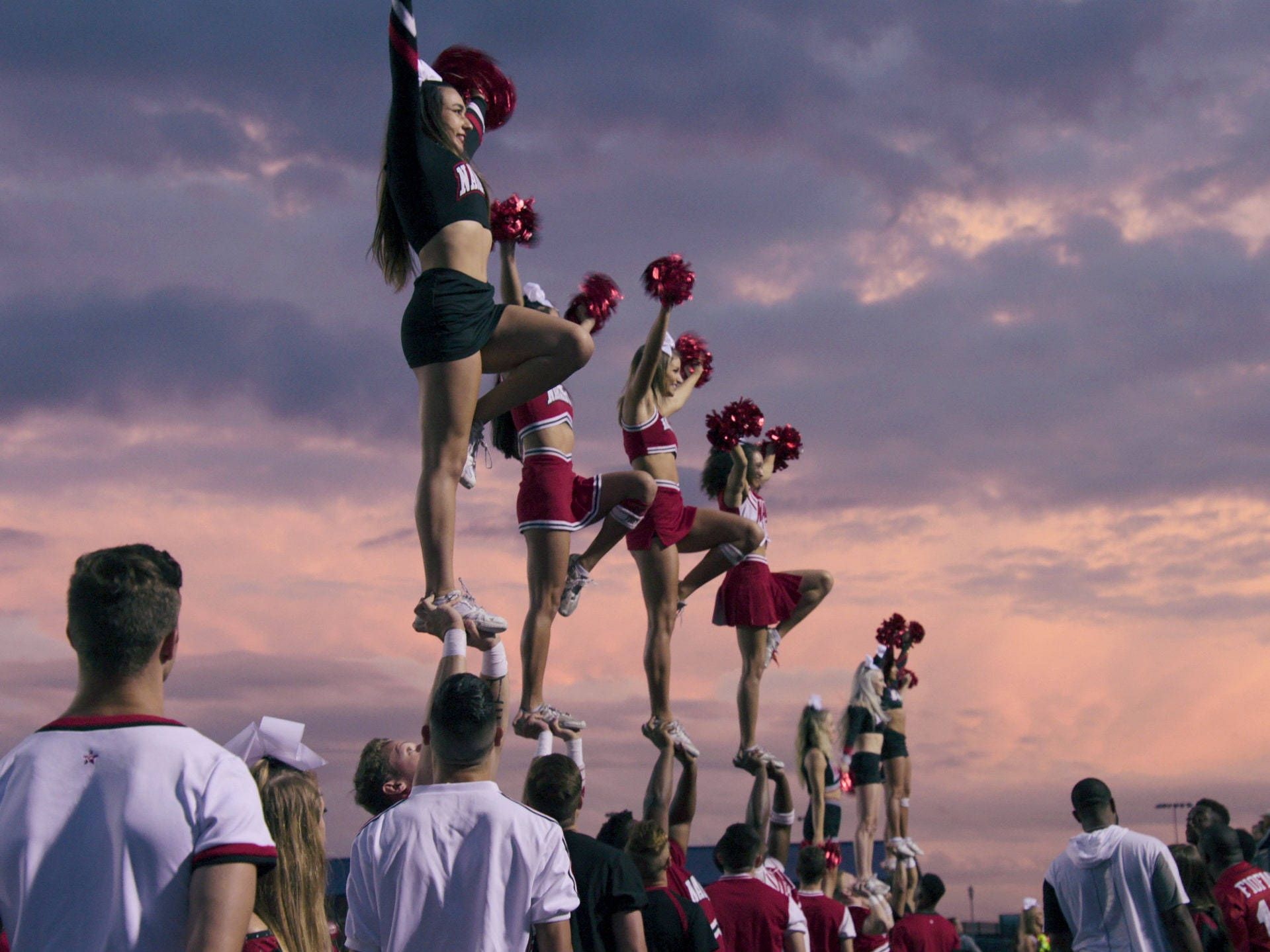 Cheerleader 桌布 壁紙 — 穿著紅色和黑色制服的啦啦隊員在戲劇性的日落天空下表演動感的金字塔特技。