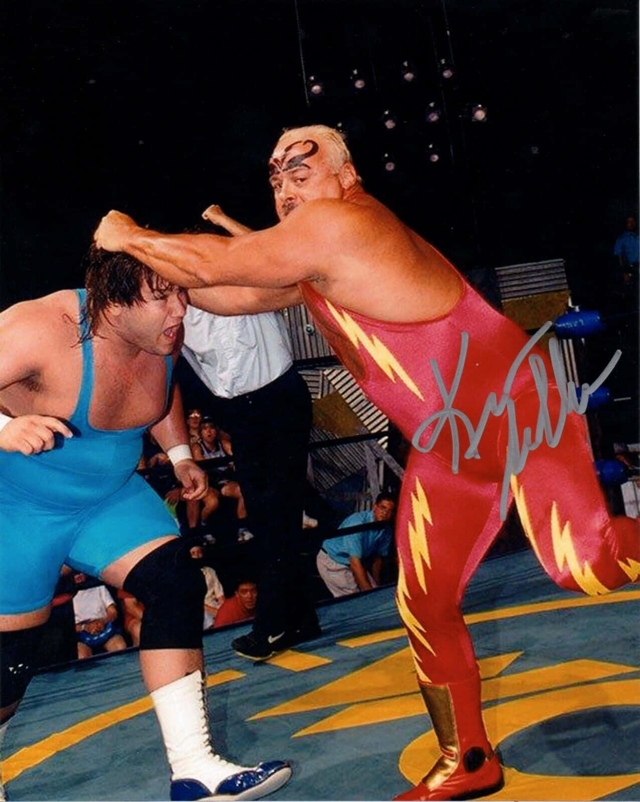WWE 桌布 壁紙 — 穿著紅色閃電服裝的摔角手在競技場燈光下與穿著藍色緊身衣的對手進行激烈比賽。