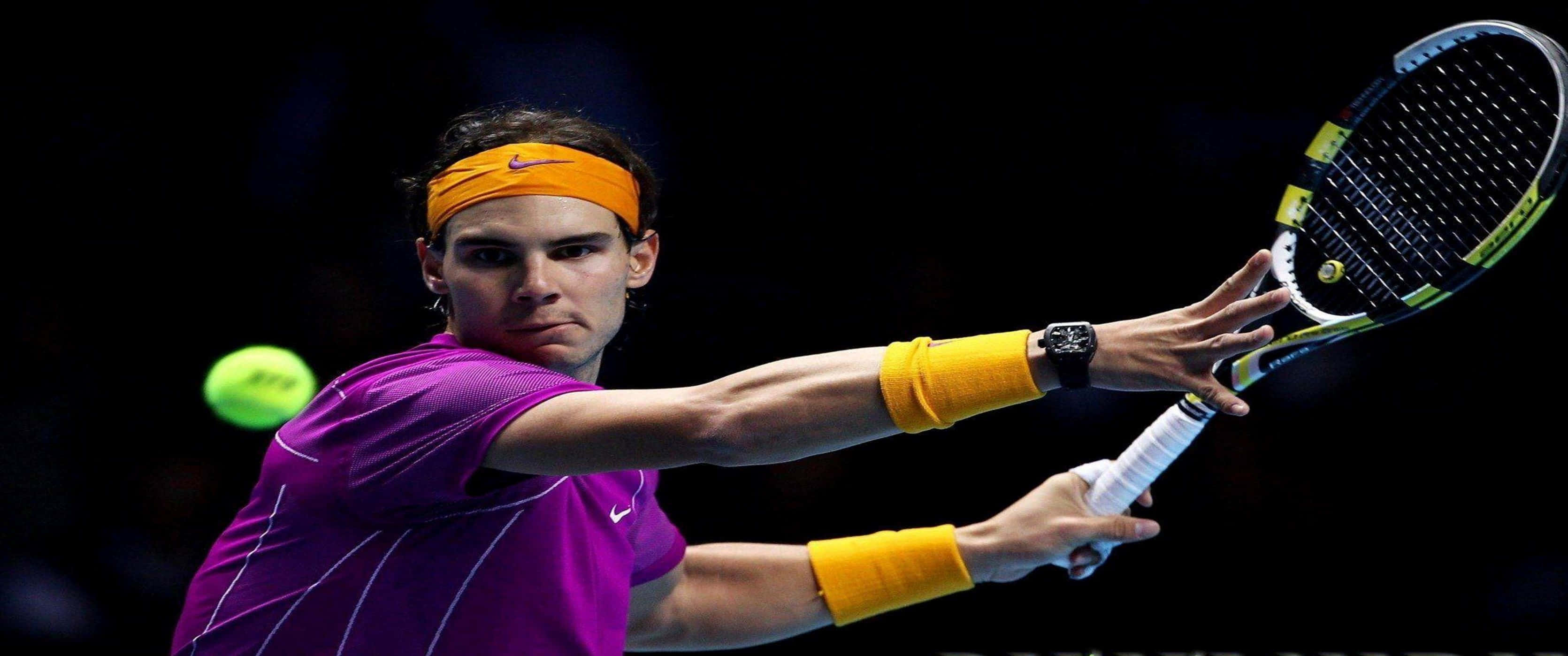 3440x1440p Tennis 桌布 壁紙 — 穿著紫色襯衫和橙色頭帶的網球選手在深色背景下揮拍擊向發光的綠色球。