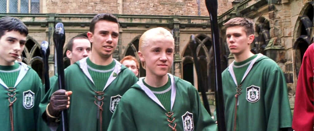 The Hogwarts Quidditch Team 桌布 壁紙 — 穿著綠色史萊哲林長袍的魁地奇球員站在石頭庭院中，手持掃帚。