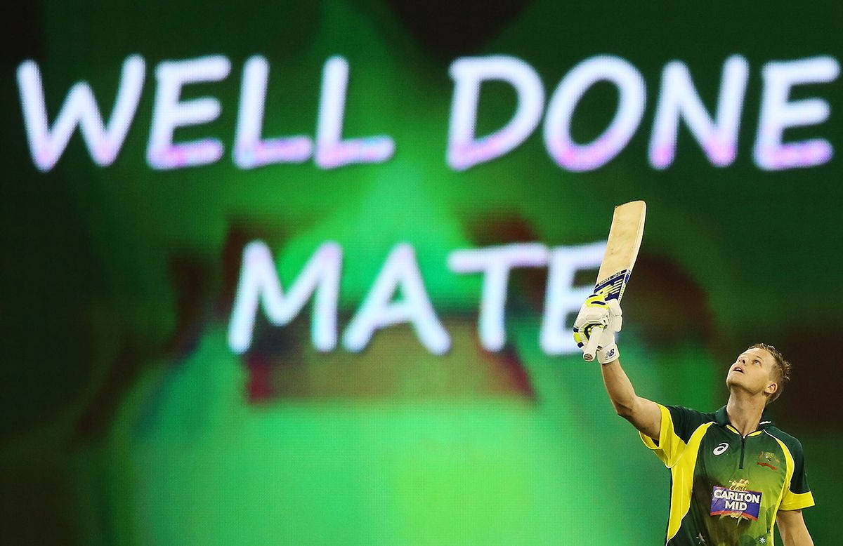 Steve Smith 桌布 壁紙 — 穿著綠色和黃色球衣的板球運動員在發光的 'WELL DONE MATE' 體育場標誌下高舉球棒慶祝勝利。