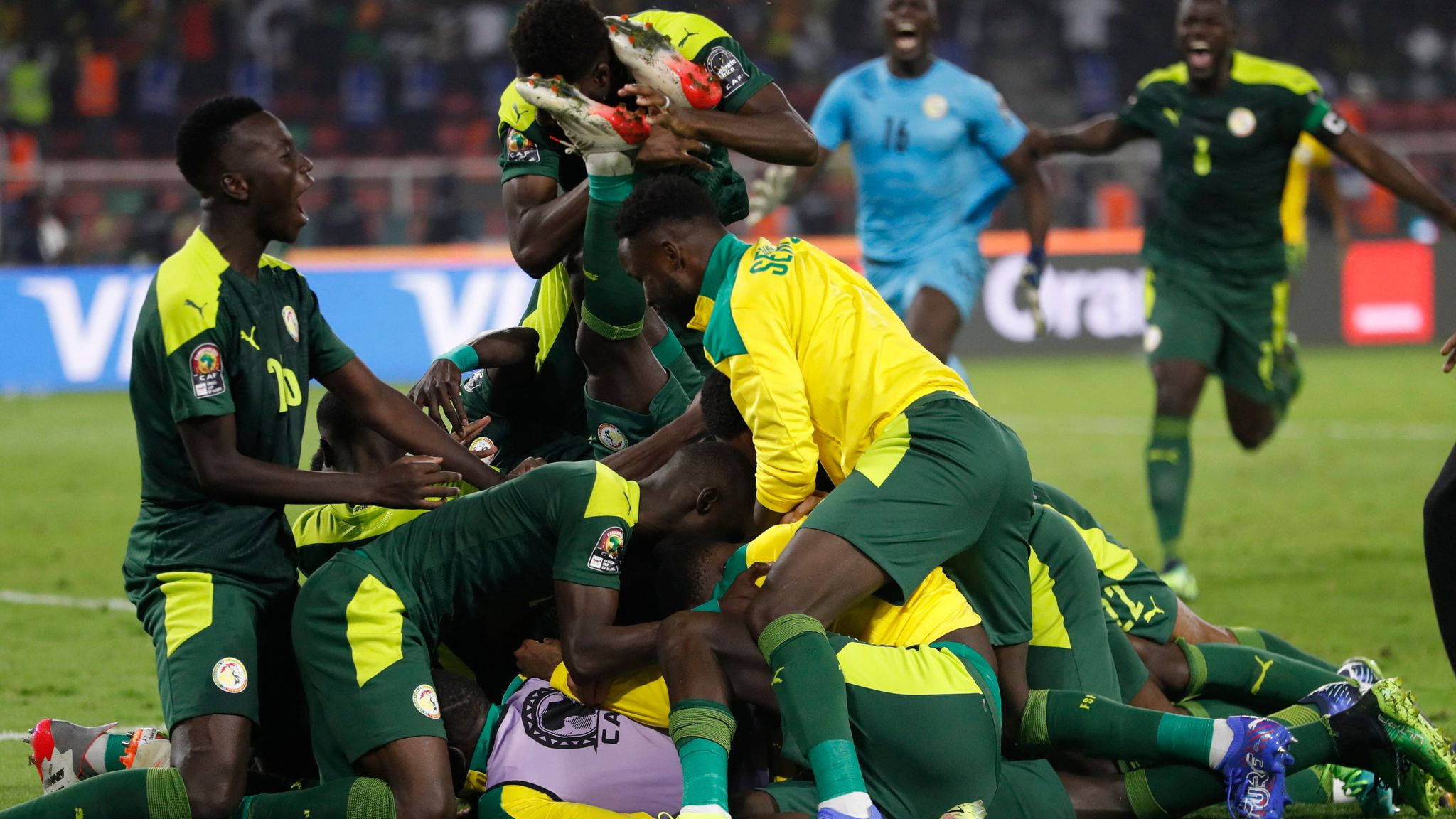 Senegal 桌布 壁紙 — 穿著綠色和黃色球衣的足球運動員在體育場上堆成一個歡樂的堆疊慶祝進球。