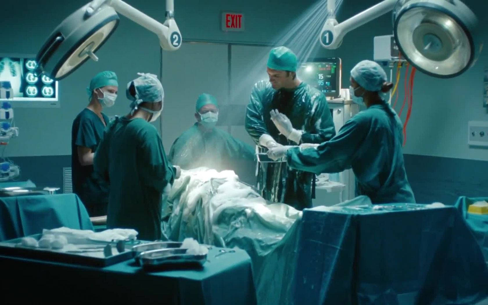 Surgeon 桌布 壁紙 — 穿著綠色手術衣和口罩的外科醫生在明亮的天花燈下於無菌手術室進行手術。