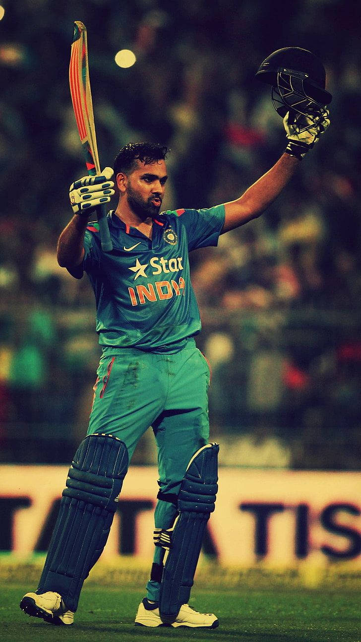 Rohit Sharma 桌布 壁紙 — 穿著綠色球衣的板球運動員在球場燈光下高舉球棒和頭盔慶祝。