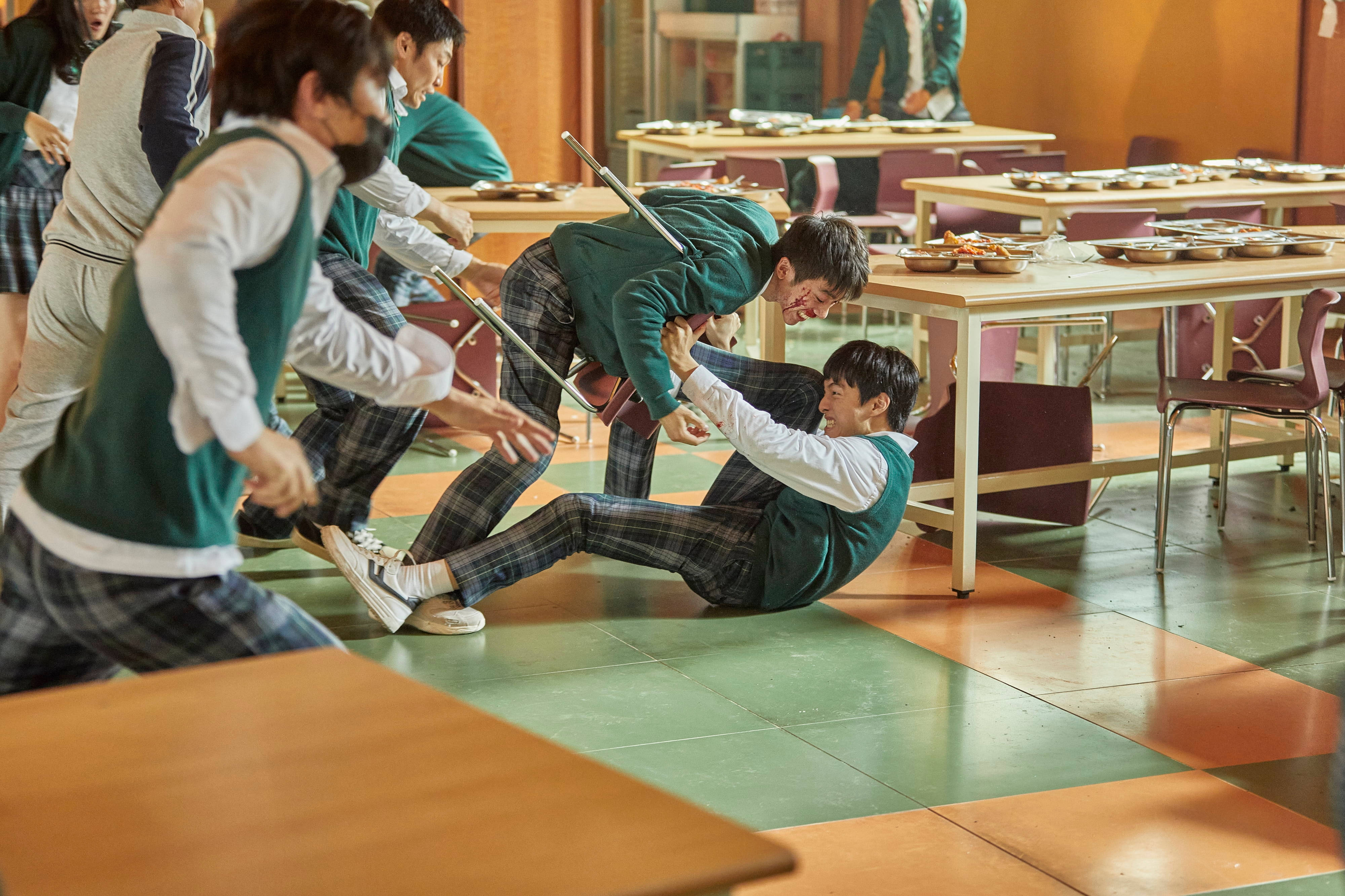 Netflix 桌布 壁紙 — 穿著綠色背心和格子褲的學生在繁忙的學校餐廳色彩繽紛的瓷磚地板上嬉戲摔跤。