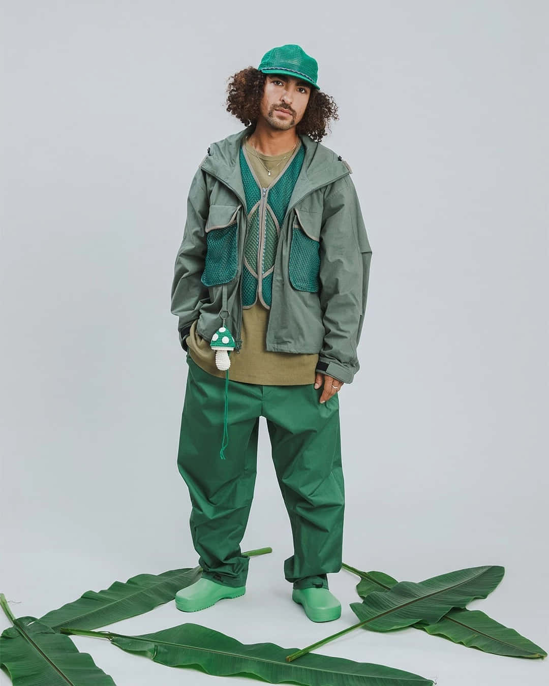 穿著綠色褲子與帽子，站在葉叢旁的男人 壁紙