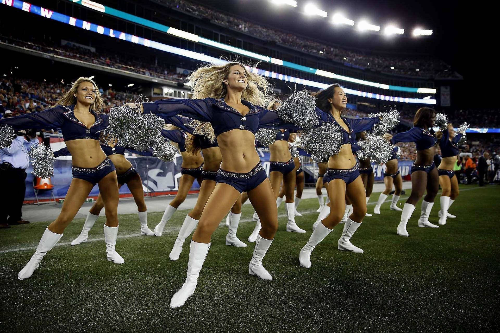 Cheerleader 桌布 壁紙 — 穿著藍色制服和白色靴子的啦啦隊員在夜間體育場燈光下用銀色彩球表演。