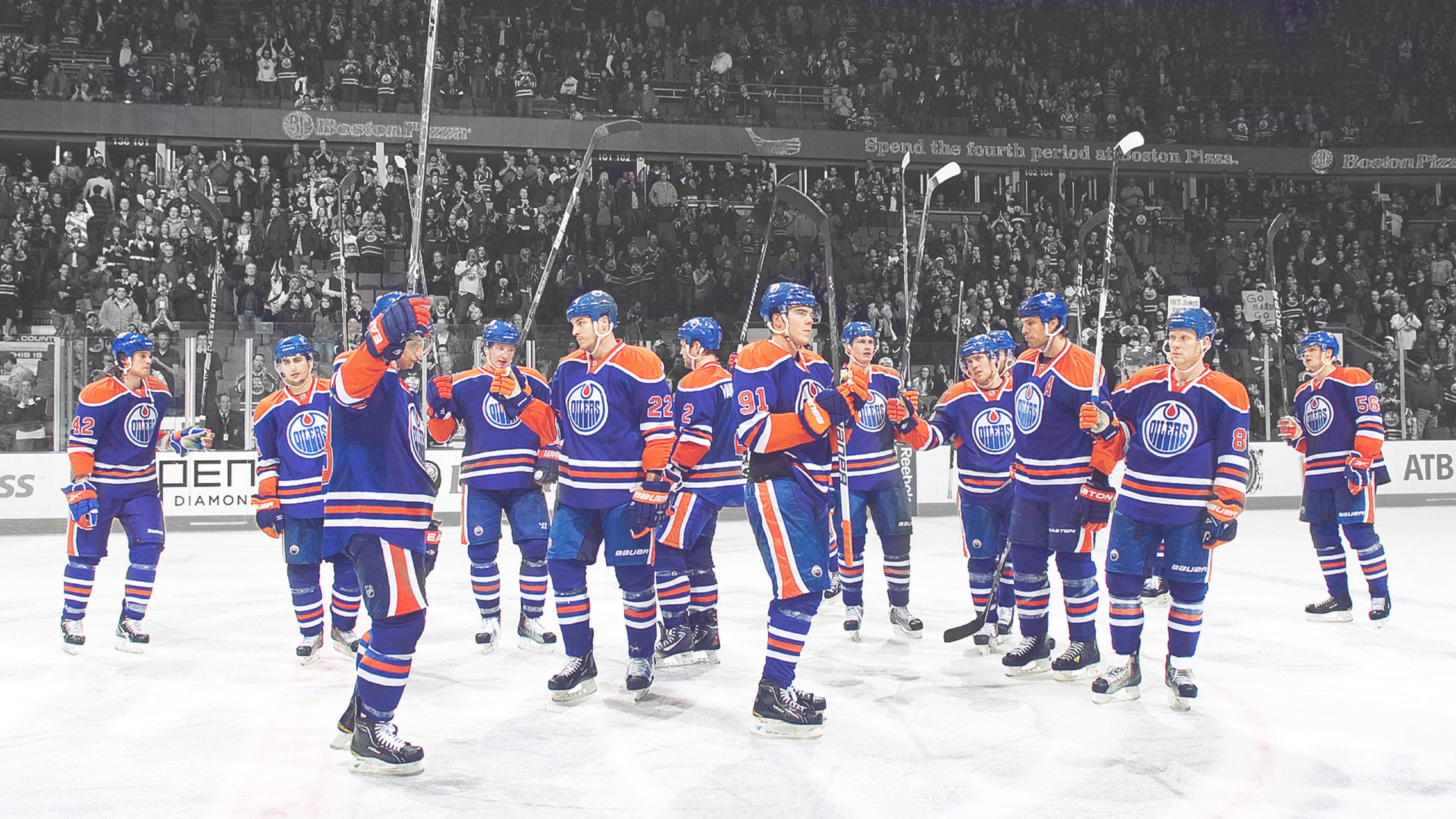 Oilers 桌布 壁紙 — 穿著藍色和橙色球衣的曲棍球運動員在冰上慶祝，背景是黑白歡呼的球迷。