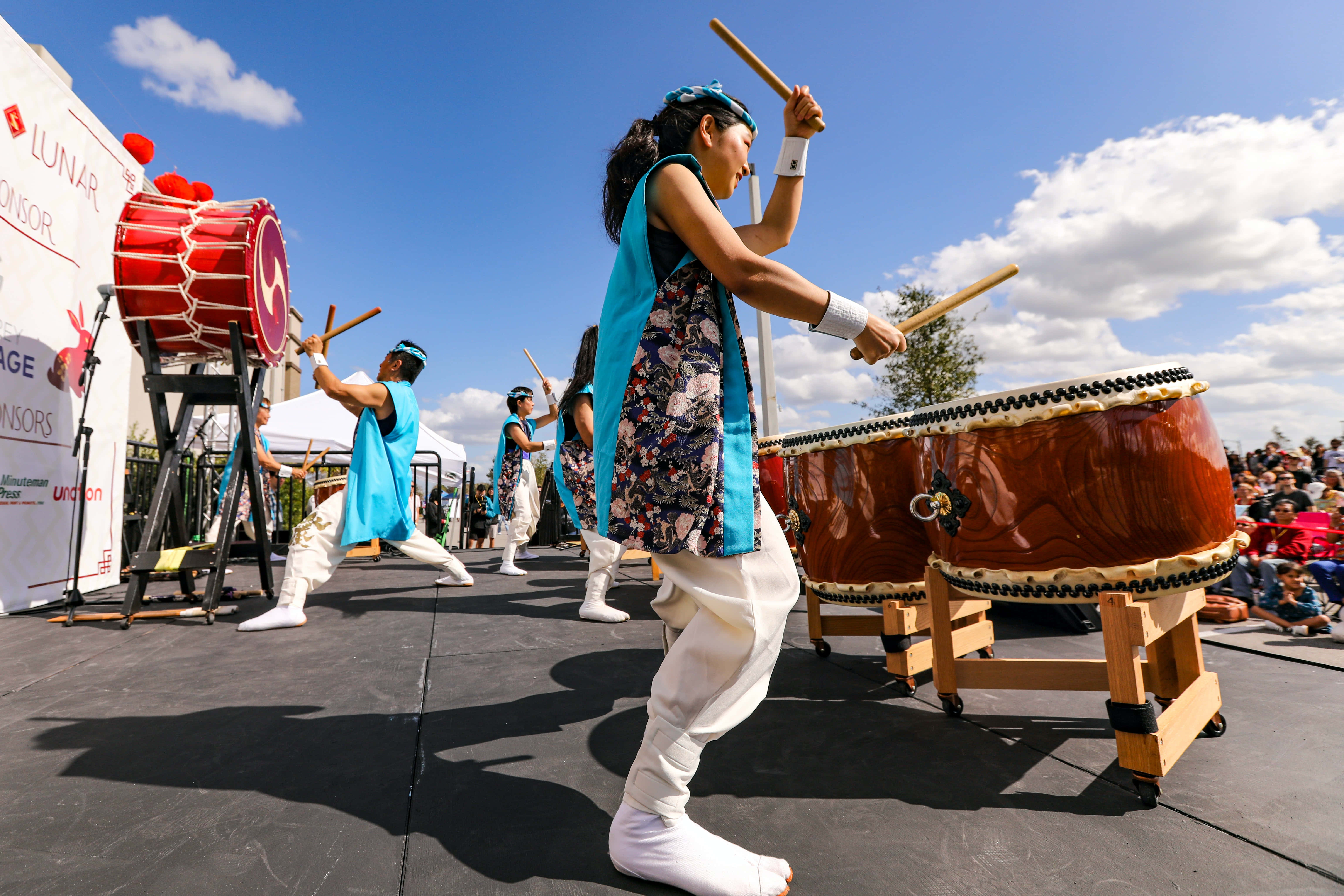 music festival 桌布 壁紙 — 穿著藍色和花卉服裝的舞者在晴朗藍天和零星白雲下，充滿活力地敲打大型太鼓。