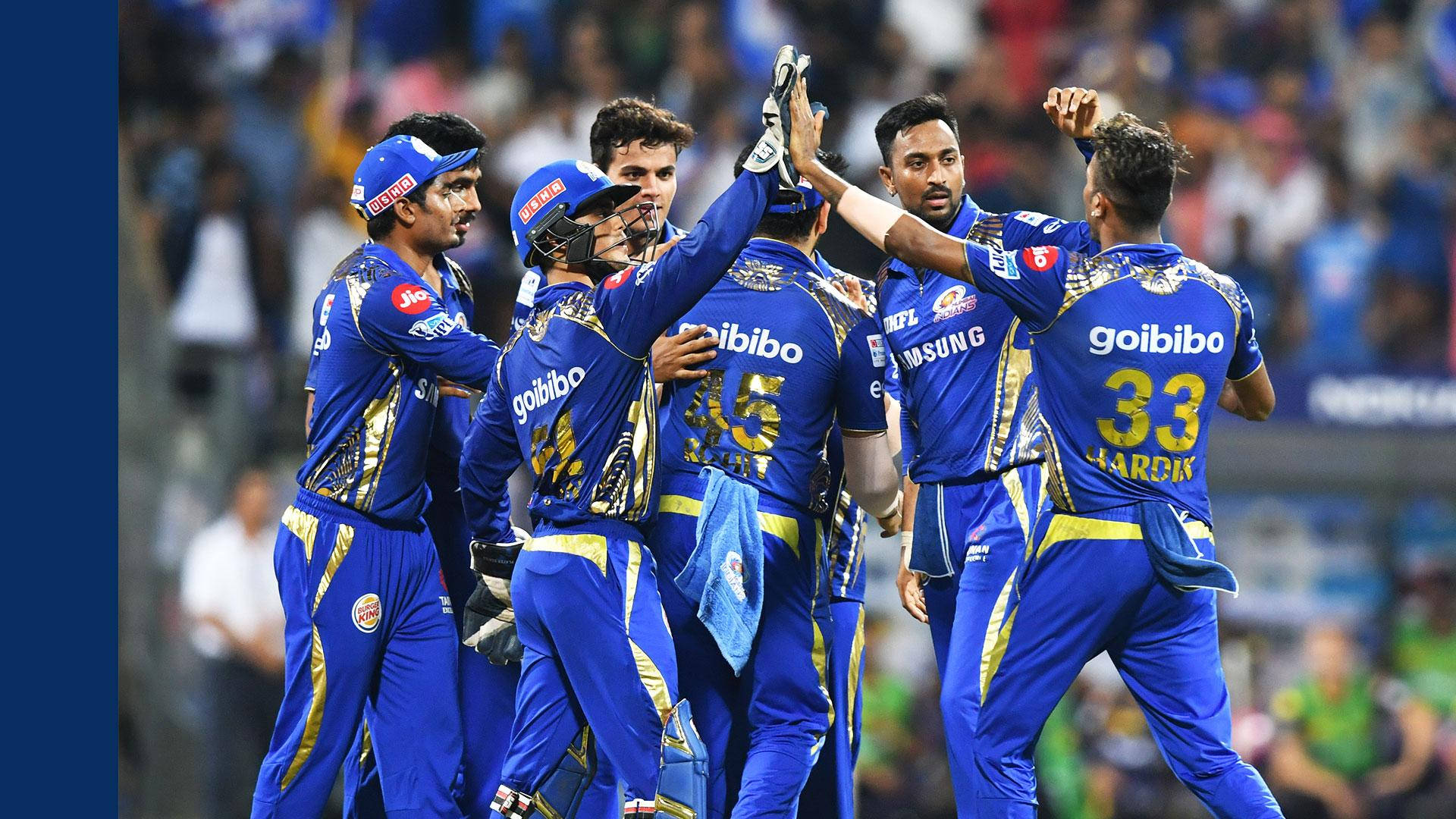 Mumbai Indians 桌布 壁紙 — 穿著藍色和金色球衣的板球運動員在體育場燈光下以擊掌和喜悅的表情慶祝勝利。