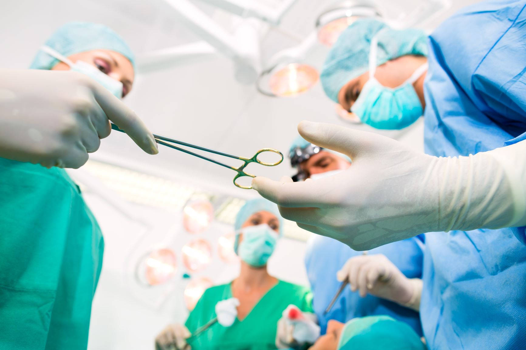 Medical 桌布 壁紙 — 穿著藍色手術服和口罩的外科醫生在光線明亮的手術室中合作，專注地傳遞手術鉗。