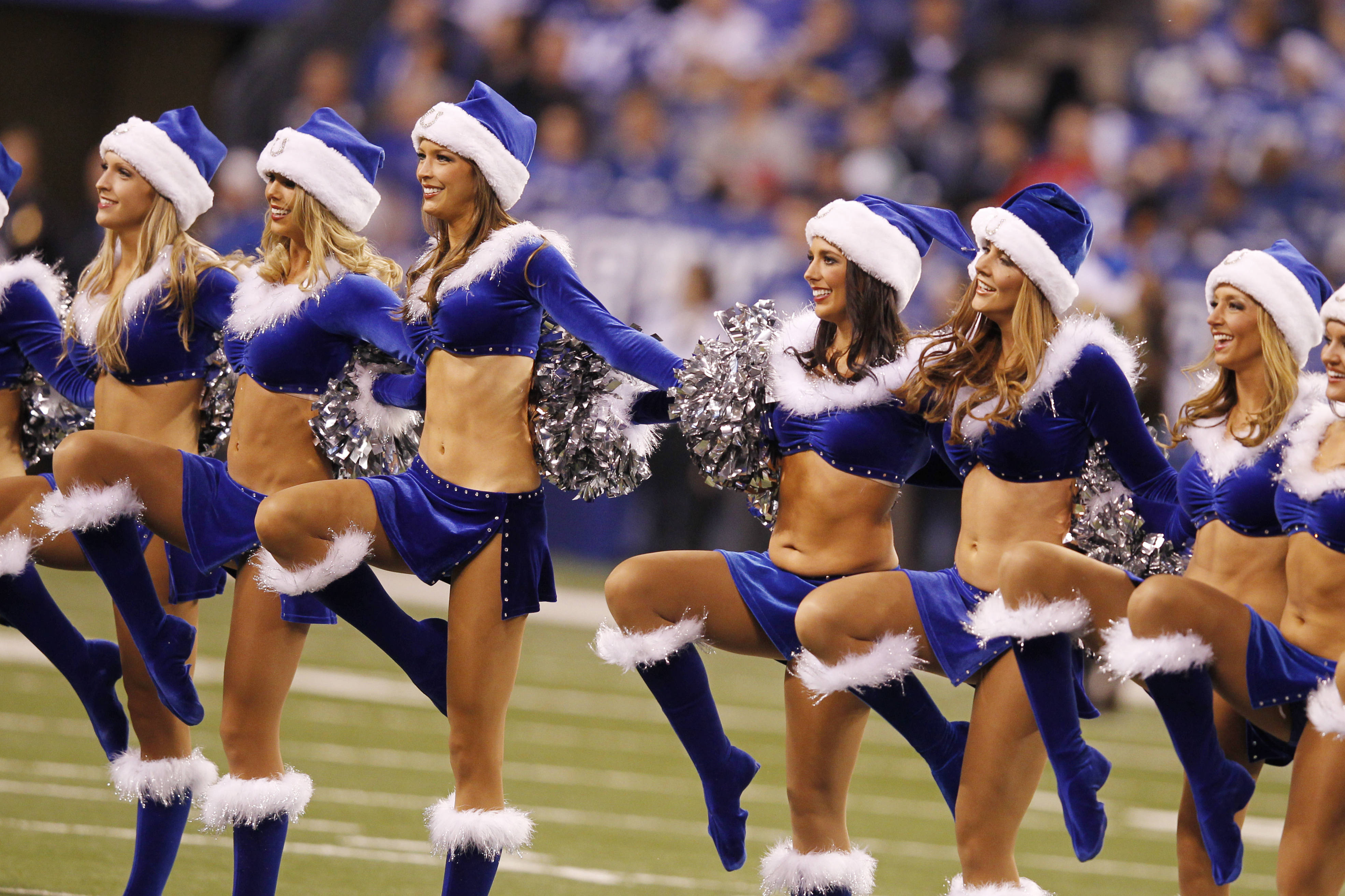 Cheerleader 桌布 壁紙 — 穿著藍色聖誕老人服裝的啦啦隊在體育場燈光下的足球場上表演同步舞蹈動作。