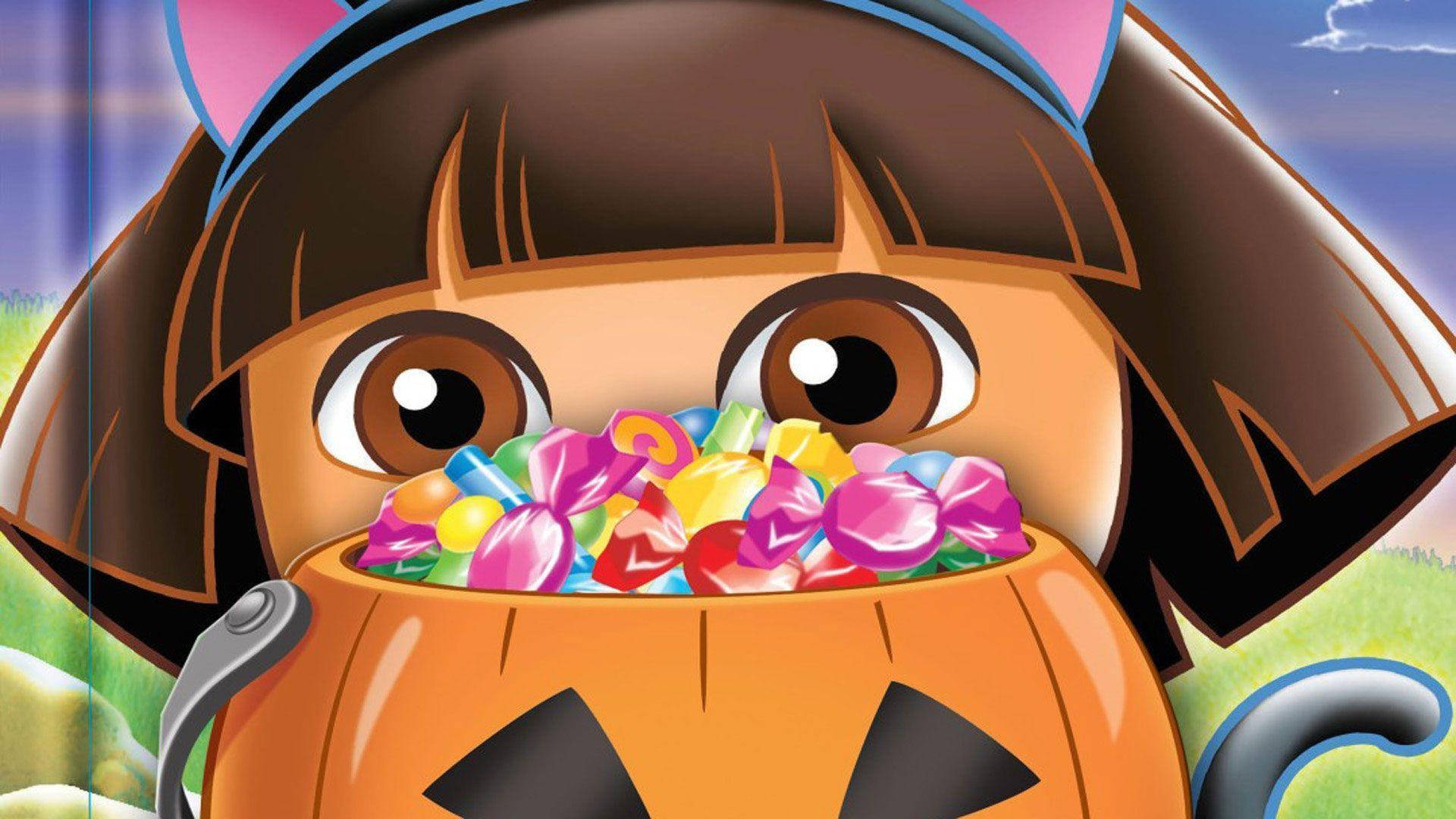 Dora 桌布 壁紙 — 穿著貓咪服裝的愛探險的朵拉拿著一個裝滿五顏六色萬聖節糖果的南瓜桶。