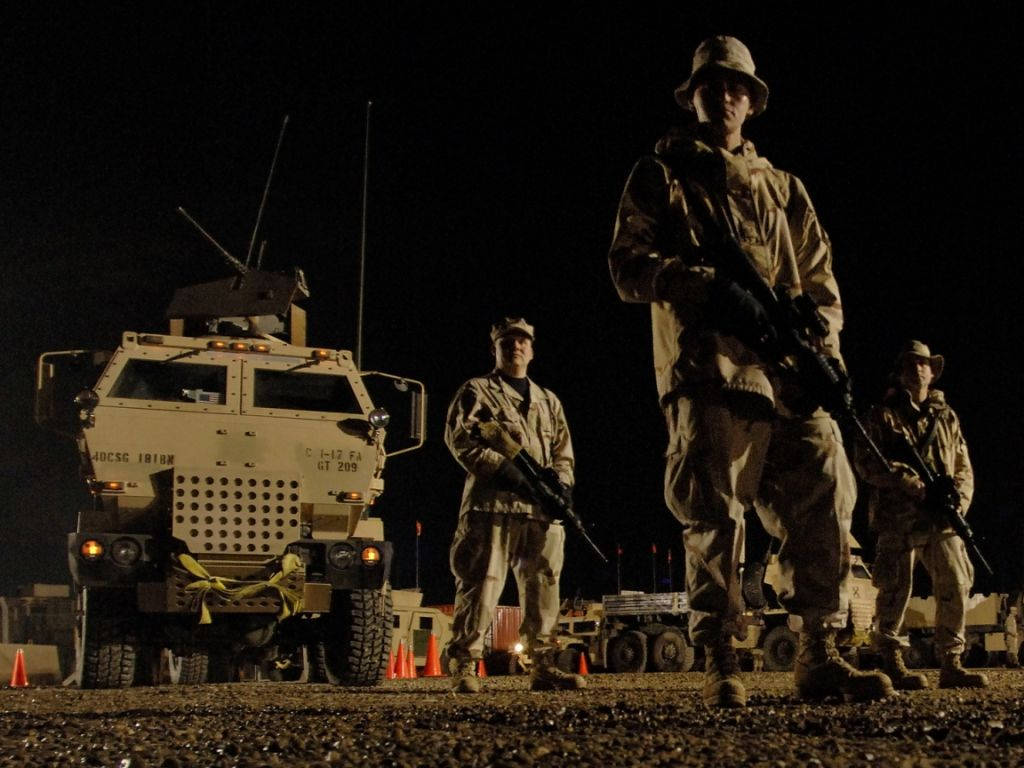 軍事動圖 桌布 壁紙 — 穿著迷彩服的士兵在夜間於人造燈光下，在裝甲車旁保持警覺。