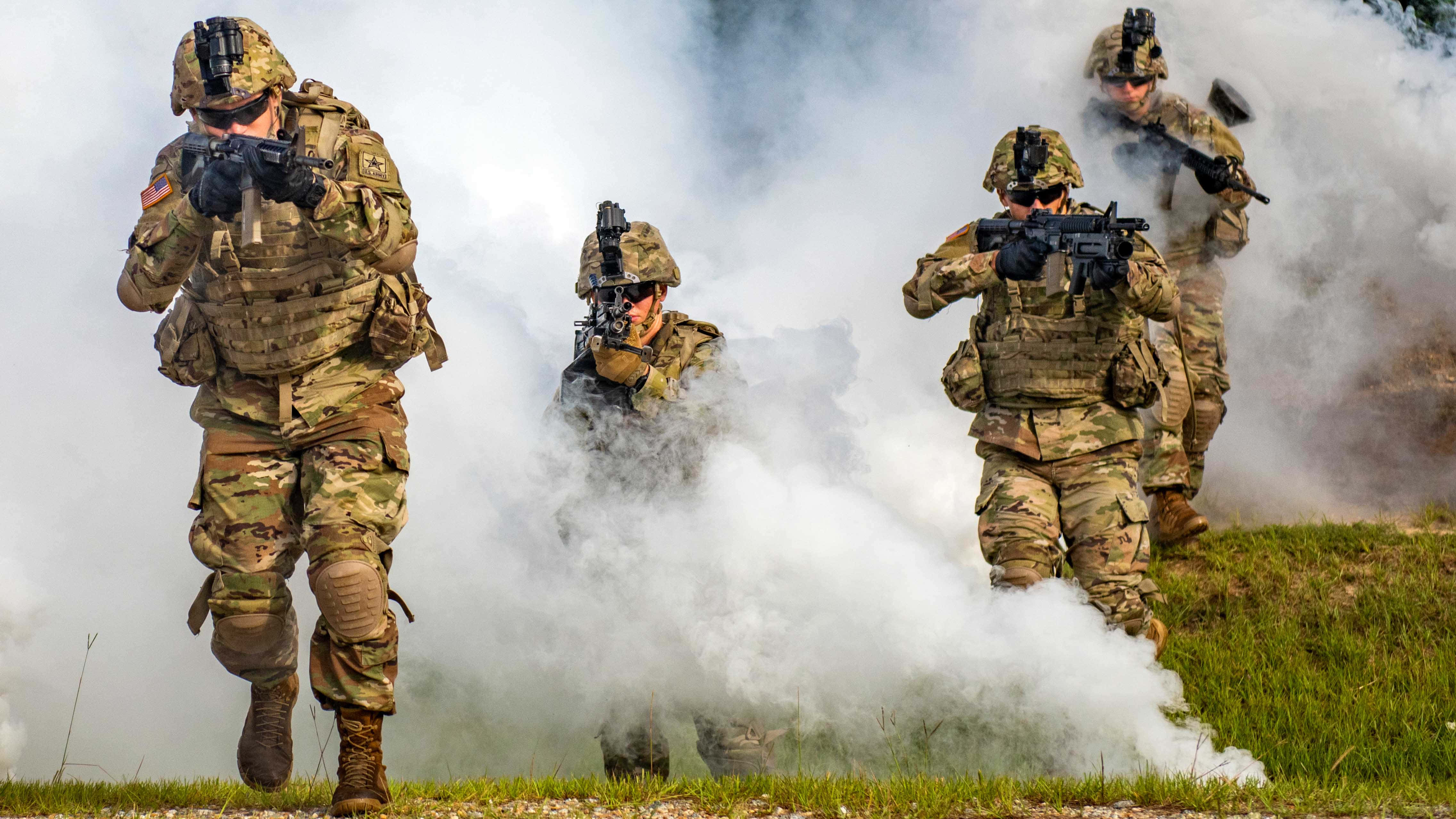 squad 桌布 壁紙 — 穿著迷彩裝備的士兵在戰術演練期間穿過草地上的濃煙前進。