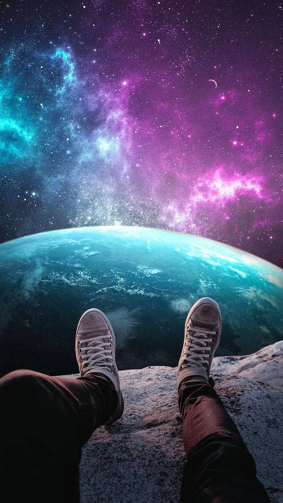 桌布 壁紙 — 穿著運動鞋的雙腳擱在岩石突出處，俯瞰著充滿活力的宇宙星雲和地球彎曲的地平線。