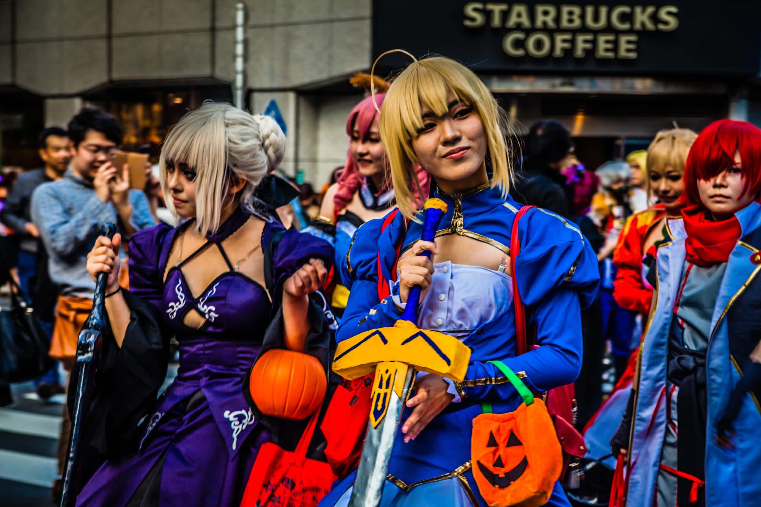 Halloween Parades 桌布 壁紙 — 穿著鮮豔萬聖節服裝的角色扮演者在星巴克店鋪附近的城市街道上愉快地擺姿勢。