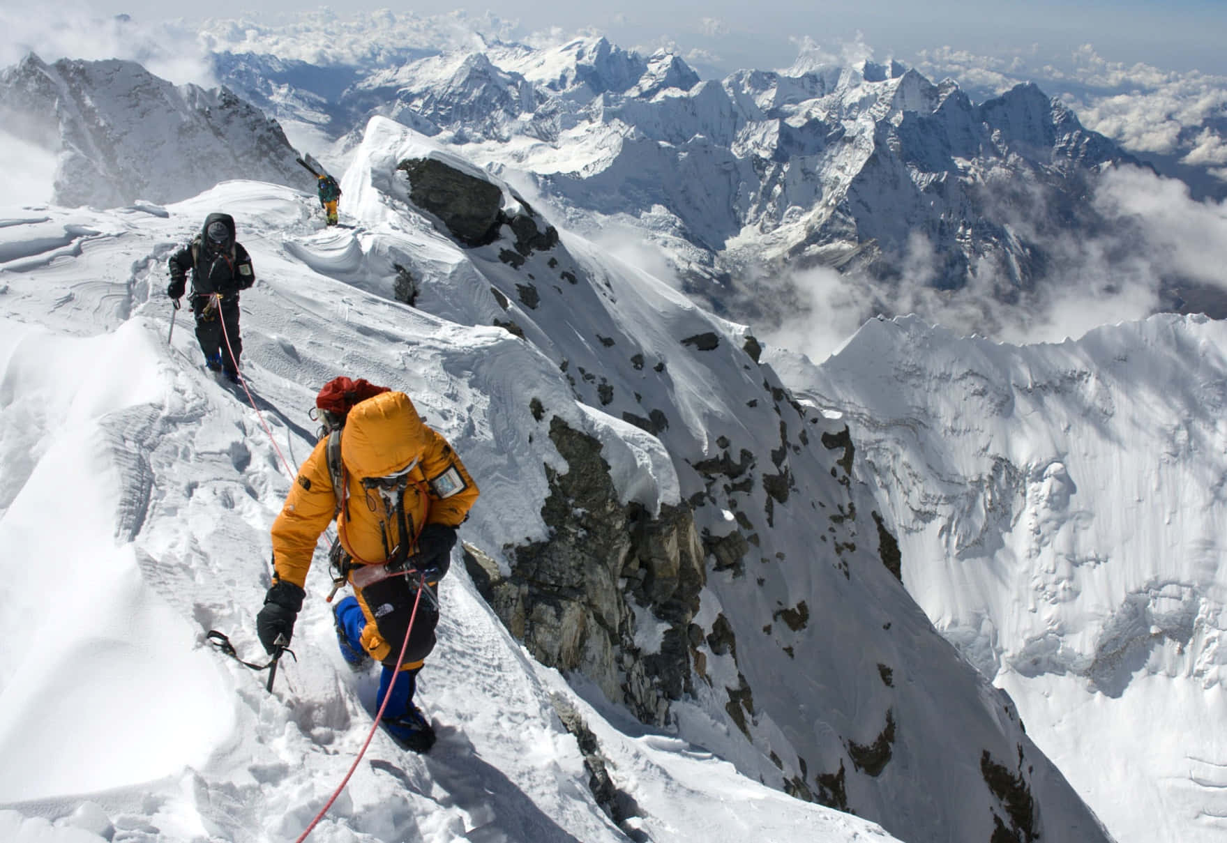 Mount Everest 桌布 壁紙 — 穿著鮮豔裝備的登山者正在攀登一條危險的積雪山脊，下方是鋸齒狀山峰和雲層。