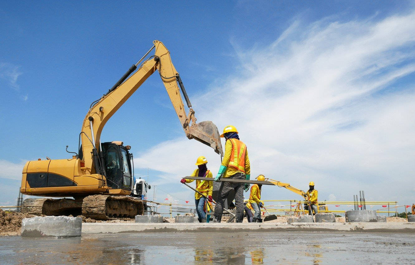 Working 桌布 壁紙 — 穿著黃色背心的建築工人在一台大型黃色挖土機旁邊操作鋼筋，背景是明亮的藍天和縷縷白雲。